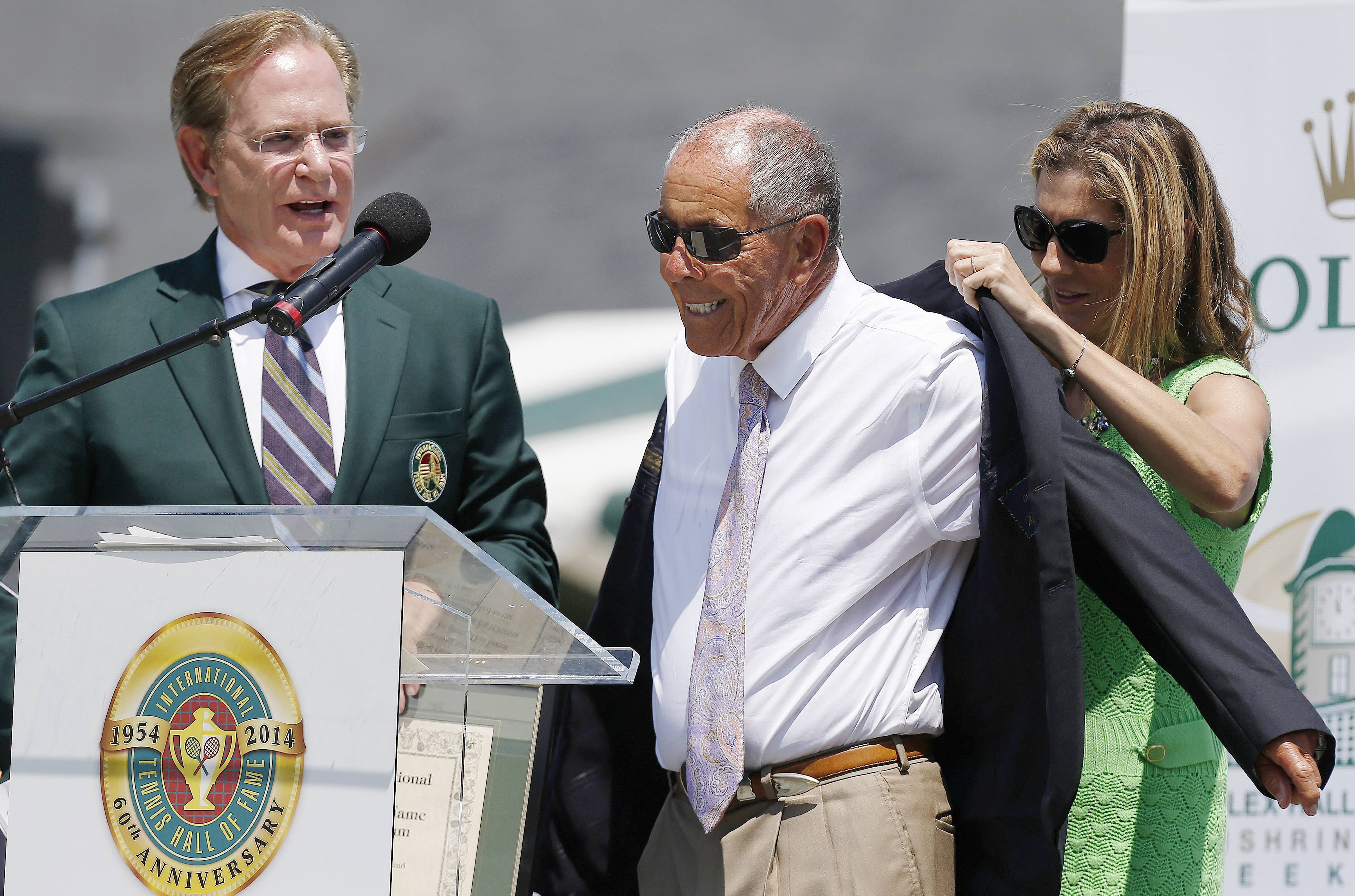 FILE - Monica Seles, right, helps Nick Bollettieri with a blazer as Hall of Fame chairman of the board Christopher Clouser, left, looks on during Bollettieri's induction into the International Tennis Hall of Fame in Newport, R.I., Saturday, July 12, 2014. Nick Bollettieri, the Hall of Fame tennis coach who worked with some of the sport’s biggest stars and founded an academy that revolutionized the development of young athletes, has died. He was 91. Bollettieri passed away Sunday night, Dec. 4, 2022, at home in Florida after a series of health issues, his manager, Steve Shulla, said in a telephone interview with The Associated Press on Monday. 