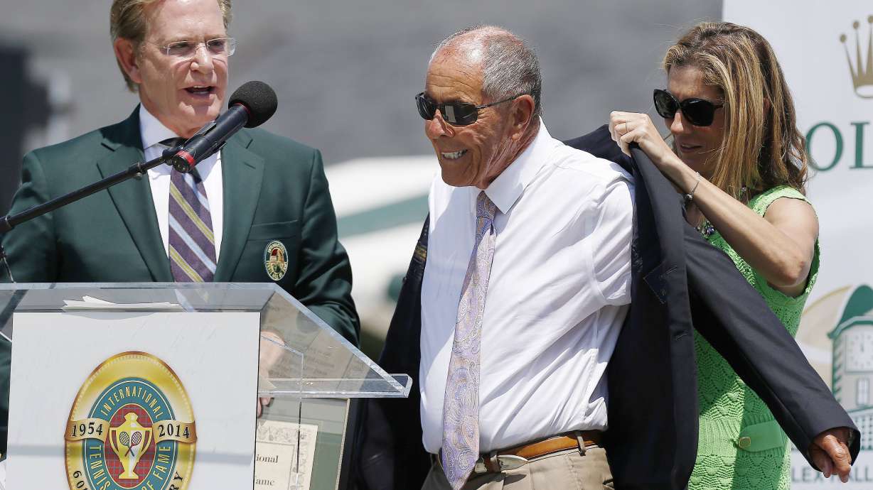 FILE - Monica Seles, right, helps Nick Bollettieri with a blazer as Hall of Fame chairman of the board Christopher Clouser, left, looks on during Bollettieri's induction into the International Tennis Hall of Fame in Newport, R.I., Saturday, July 12, 2014. Nick Bollettieri, the Hall of Fame tennis coach who worked with some of the sport’s biggest stars and founded an academy that revolutionized the development of young athletes, has died. He was 91. Bollettieri passed away Sunday night, Dec. 4, 2022, at home in Florida after a series of health issues, his manager, Steve Shulla, said in a telephone interview with The Associated Press on Monday.