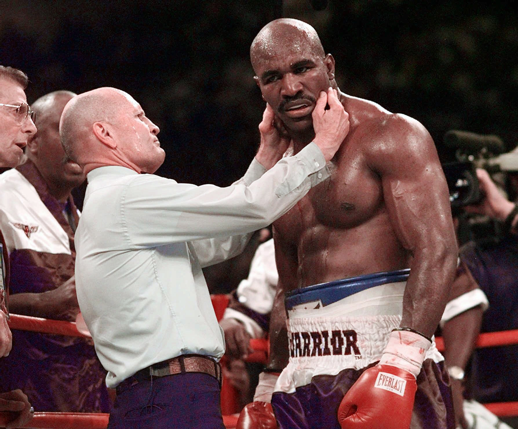 FILE - Evander Holyfield has his right ear checked by referee Mills Lane after he was bit on the ear by Mike Tyson during the third round of their WBA heavyweight boxing match June 28, 1997, in Las Vegas. Lane, the Hall of Fame boxing referee who was the third man in the ring when Tyson bit Holyfield’s ear, died Tuesday, Dec. 6, 2022. He was 85. Lane had suffered a stroke in 2002 and son Tommy said his father had taken a significant turn for the worse recently before entering hospice care Friday. 