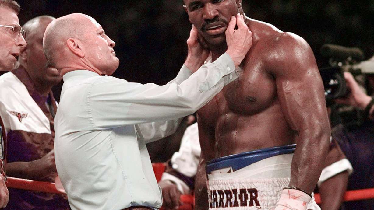 FILE - Evander Holyfield has his right ear checked by referee Mills Lane after he was bit on the ear by Mike Tyson during the third round of their WBA heavyweight boxing match June 28, 1997, in Las Vegas. Lane, the Hall of Fame boxing referee who was the third man in the ring when Tyson bit Holyfield’s ear, died Tuesday, Dec. 6, 2022. He was 85. Lane had suffered a stroke in 2002 and son Tommy said his father had taken a significant turn for the worse recently before entering hospice care Friday.