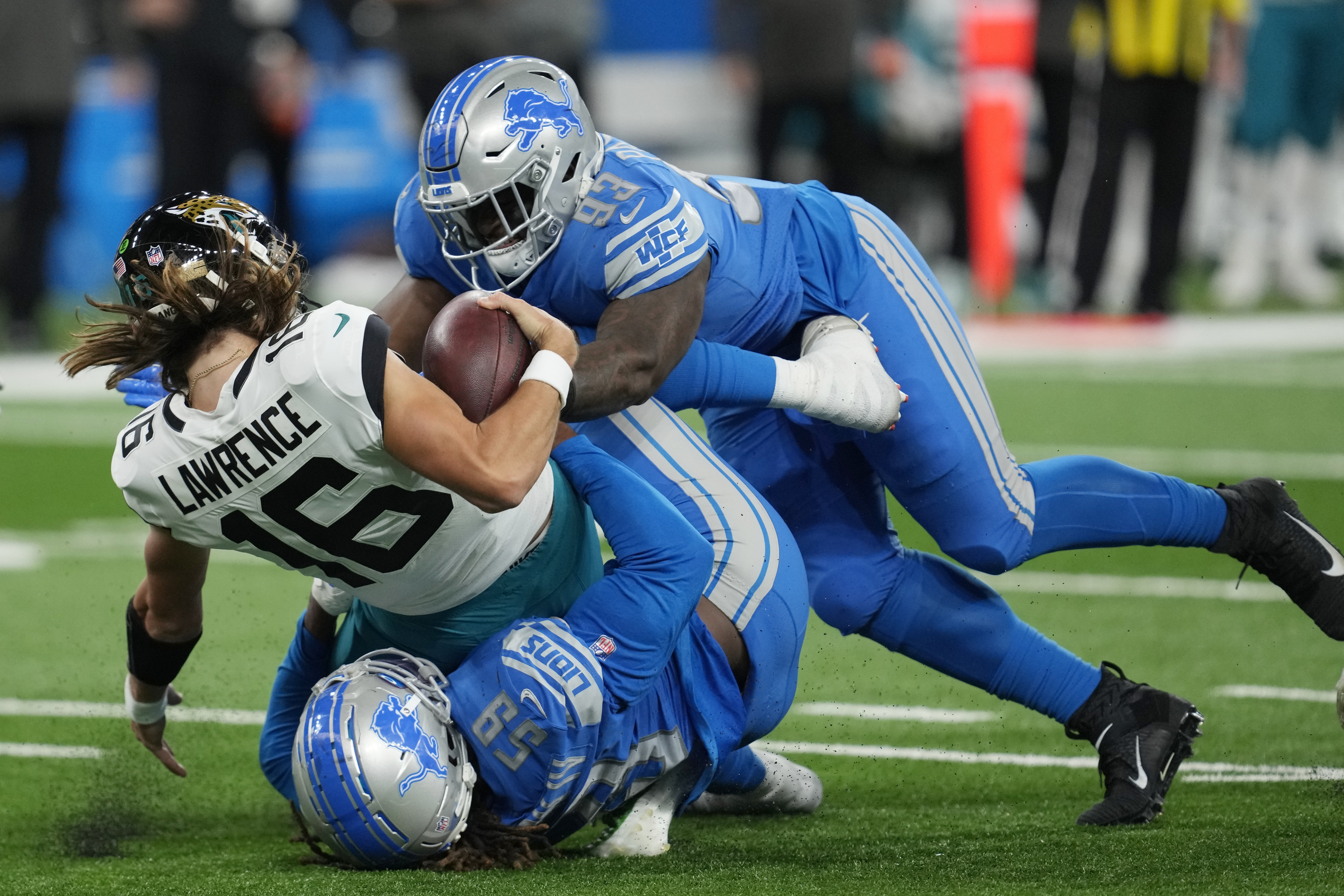 Jacksonville Jaguars quarterback Trevor Lawrence (16) is sacked by Detroit Lions linebacker James Houston (59) and defensive end Josh Paschal (93) during the first half of an NFL football game, Sunday, Dec. 4, 2022, in Detroit.