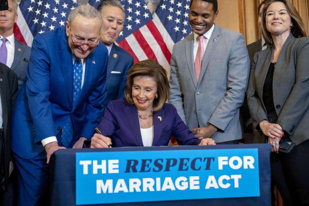 House Speaker Nancy Pelosi of Calif., accompanied by Senate Majority Leader Sen. Chuck Schumer of N.Y., left, and other members of Congress, signs the H.R. 8404, the Respect For Marriage Act, on Capitol Hill in Washington, Thursday.