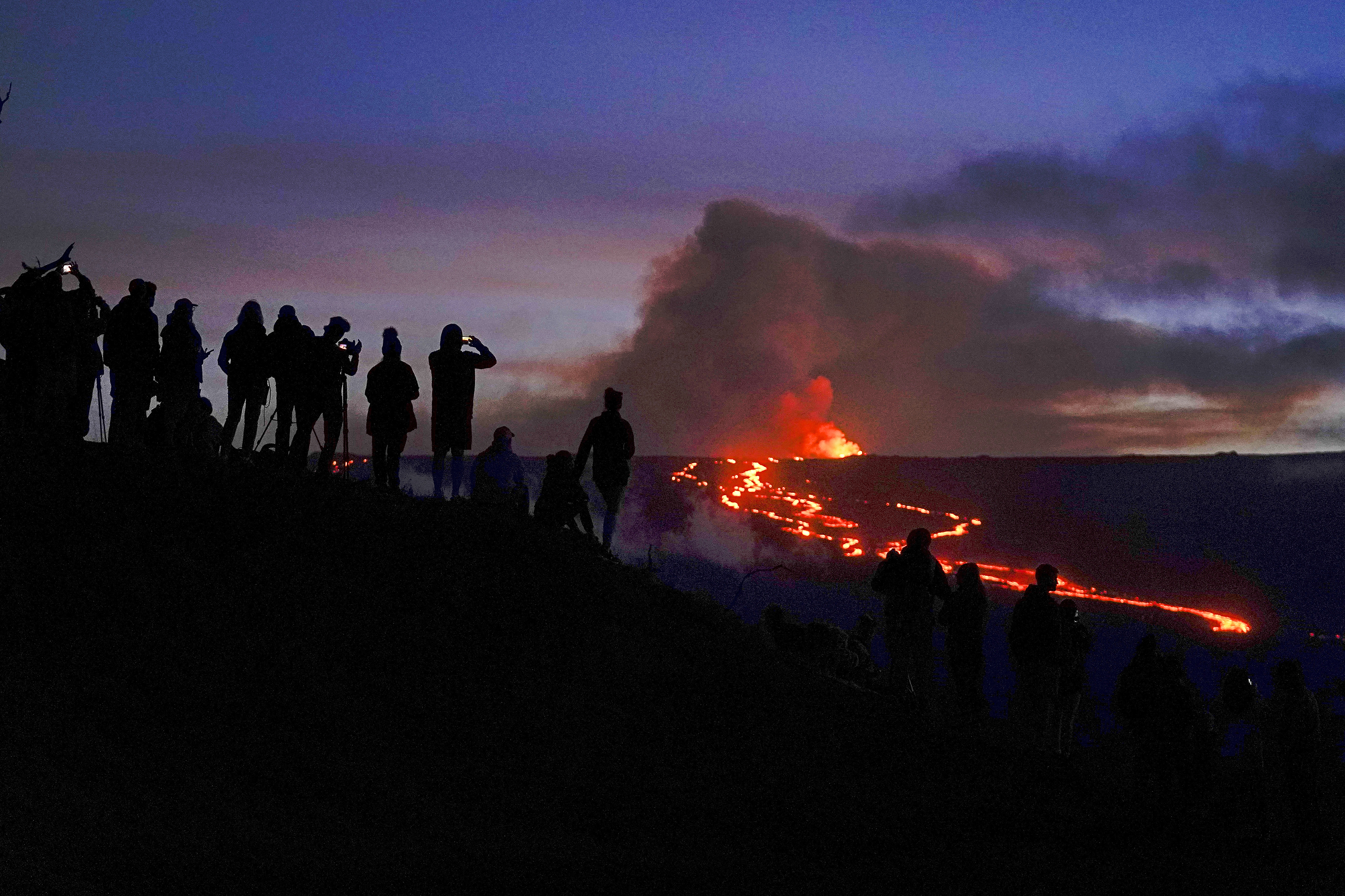 People watch and record images of lava from the Mauna Loa volcano Dec. 1, near Hilo, Hawaii. The U.S. Geological Survey said Thursday that Mauna Loa is still erupting but lava that was feeding the flow heading toward the road has been cut off.