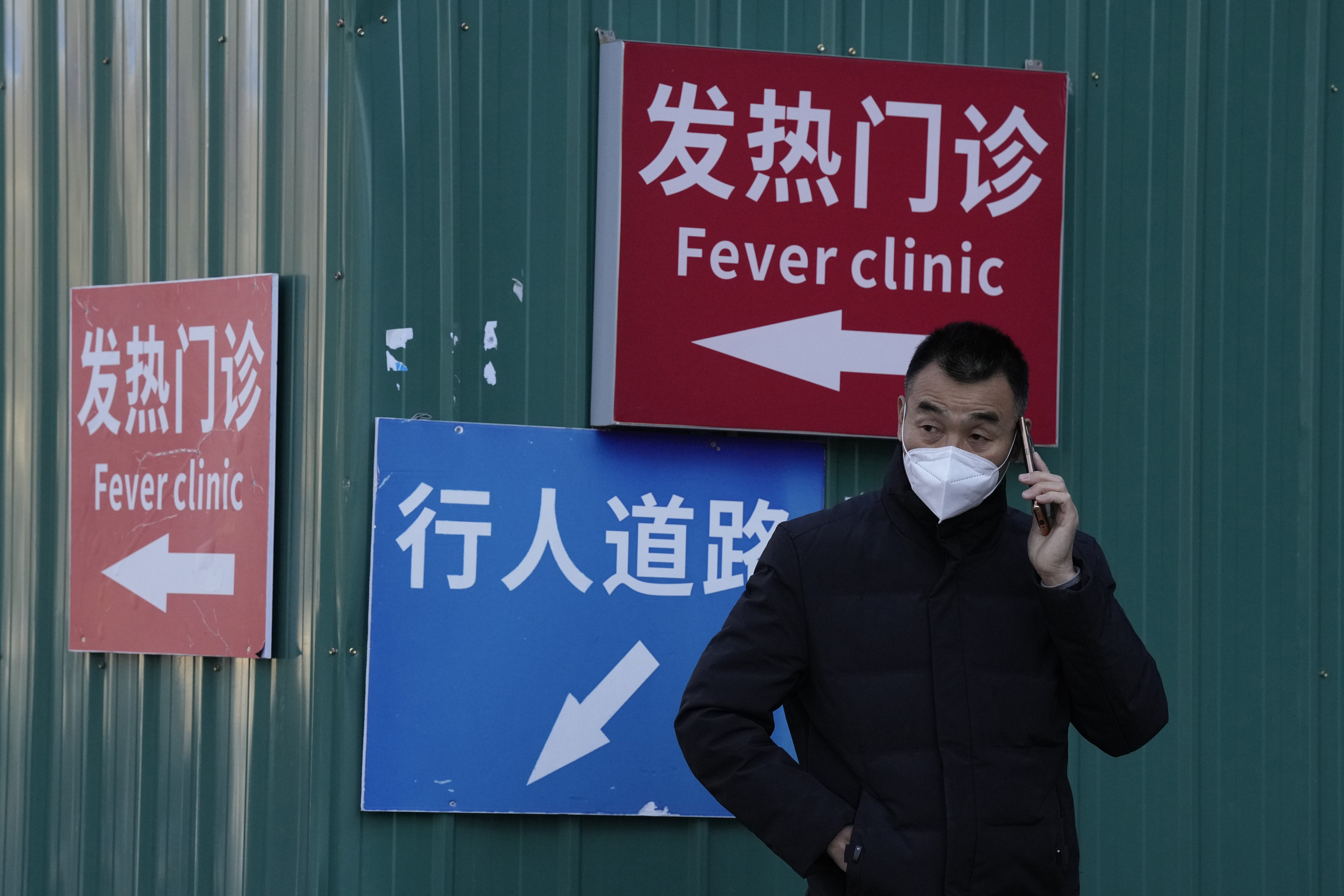A man wearing a mask talks on his phone near signs directing visitors to the fever clinic at a hospital in Beijing, Saturday. A rash of COVID-19 cases in schools and businesses were reported Friday in areas across China after the ruling Communist Party loosened anti-virus rules as it tries to reverse a deepening economic slump. 