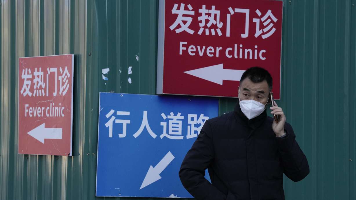 A man wearing a mask talks on his phone near signs directing visitors to the fever clinic at a hospital in Beijing, Saturday. A rash of COVID-19 cases in schools and businesses were reported Friday in areas across China after the ruling Communist Party loosened anti-virus rules as it tries to reverse a deepening economic slump.