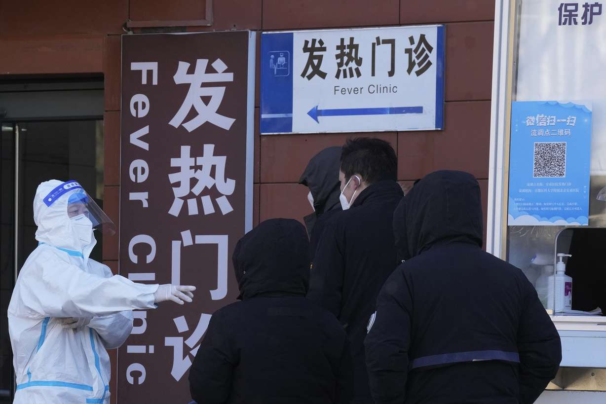 A worker in protective overalls controls the line outside the fever clinic at a hospital in Beijing, Saturday. A rash of COVID-19 cases in schools and businesses were reported Friday in areas across China after the ruling Communist Party loosened anti-virus rules as it tries to reverse a deepening economic slump.