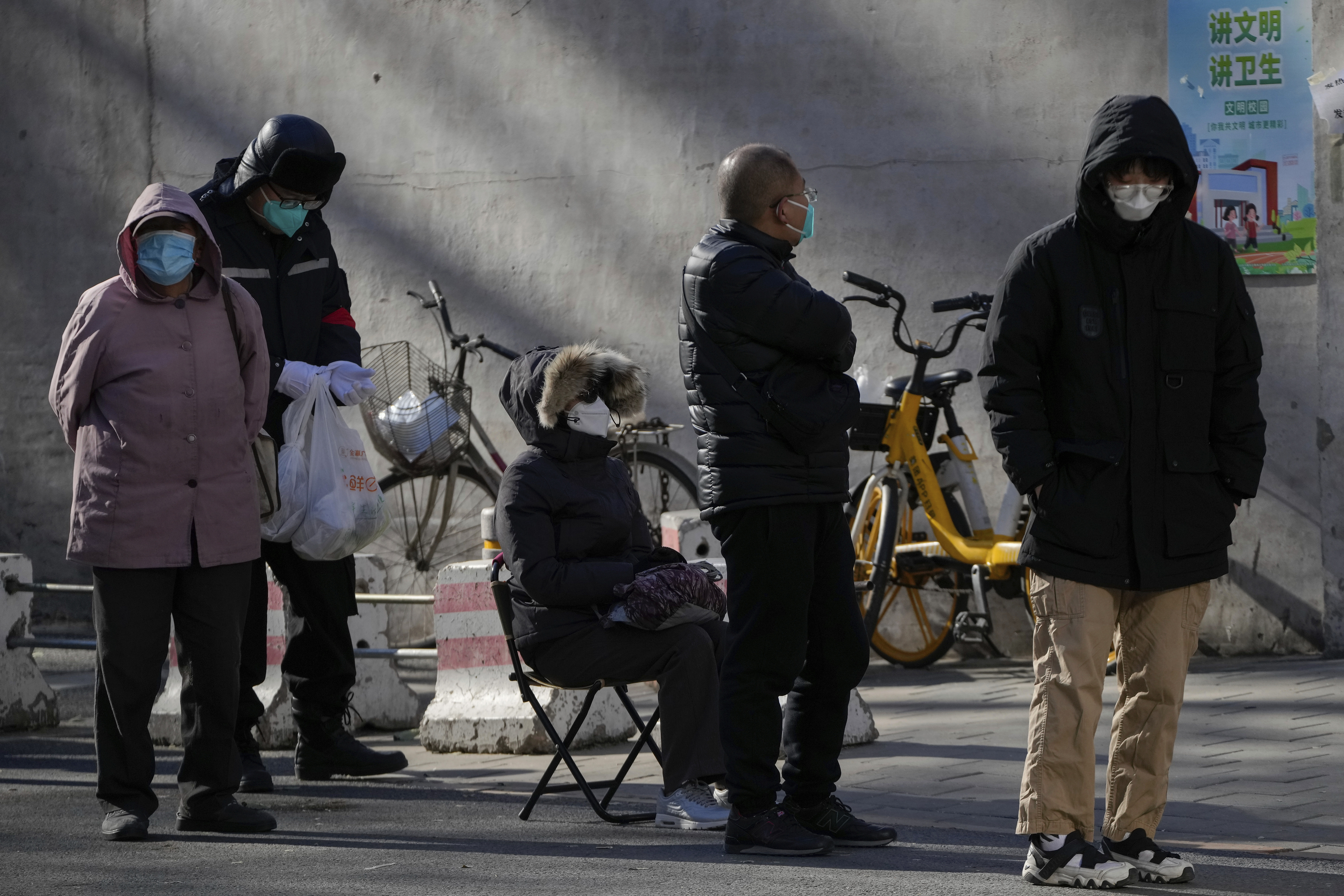 A woman sits on a foldable chair as residents wait in line to enter the fever clinic of a hospital in Beijing, Sunday. Facing a surge in COVID-19 cases, China is setting up more intensive care facilities and trying to strengthen hospitals as Beijing rolls back anti-virus controls that confined millions of people to their homes, crushed economic growth and set off protests.