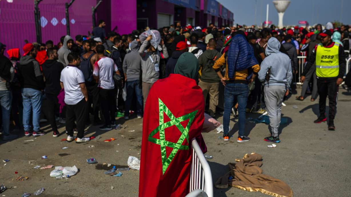 A man draped in a Moroccan flag queues with supporters outside the Al Janoub Stadium in Wakrah, Qatar on Tuesday, Dec. 13, 2022 in the hope of getting tickets for Wednesday's World Cup semifinal soccer match between France and Morocco.