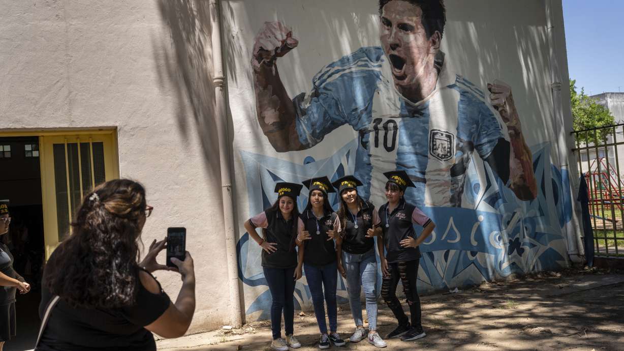 Students graduating from the General Las Heras elementary school, where Lionel Messi also attended school, pose for a group photo wearing their graduation hats by a mural of Messi, on the last day of school in Rosario, Argentina, Wednesday, Dec. 14, 2022.