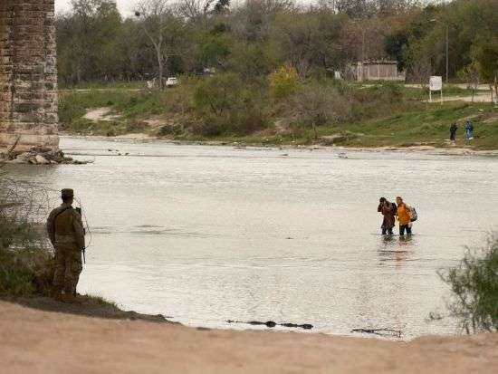 A Texas National Guardsman watches as a group of migrants wades across the Rio Grande as U.S. border cities brace for an influx of asylum seekers when COVID-era Title 42 migration restrictions were set to end, in Eagle Pass, Texas, Sunday.