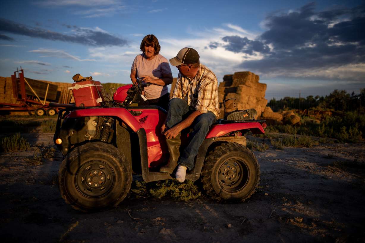 Dave Evans changes his boots while talking to his wife, Alicia Evans, before shutting off an irrigation valve at the end of the day on their property in Duchesne on July 27.