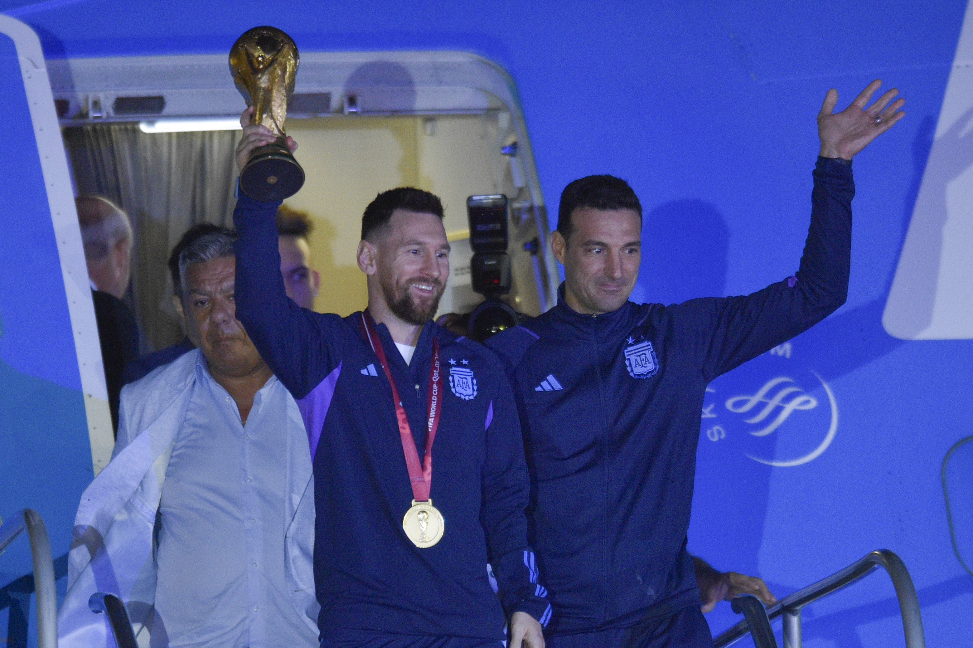 Argentina's Lionel Messi holds the FIFA World Cup trophy as he deplanes, with coach Lionel Scaloni, in Buenos Aires, Argentina, Tuesday, Dec. 20, 2022. 