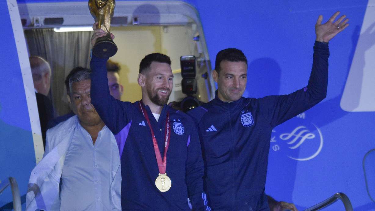 Argentina's Lionel Messi holds the FIFA World Cup trophy as he deplanes, with coach Lionel Scaloni, in Buenos Aires, Argentina, Tuesday, Dec. 20, 2022.