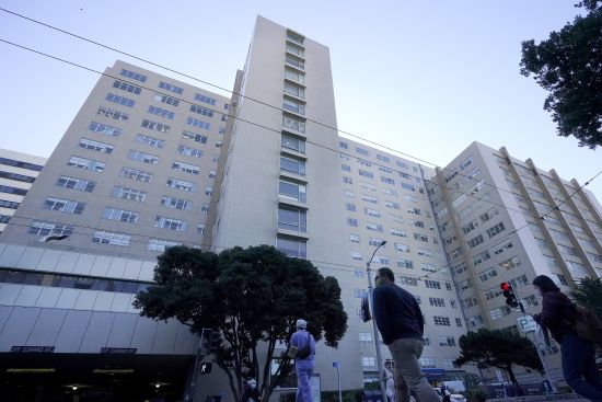 People cross the street in front of a University of California at San Francisco medical center in San Francisco on Nov. 30, 2020. A prominent California medical school has apologized for conducting unethical experimental medical treatments on 2,600 incarcerated men in the 1960s and 1970s.