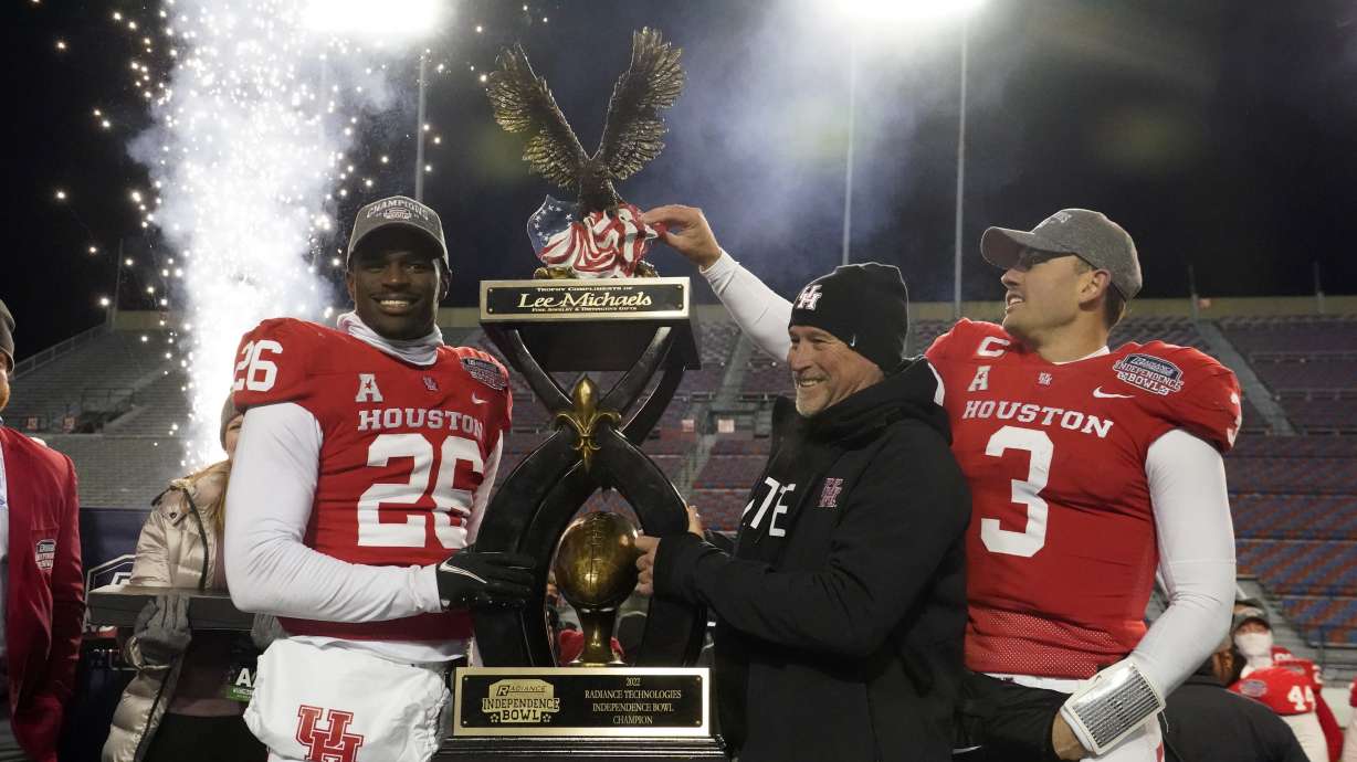 CORRECTS TO ART GREEN NOT MOSES ALEXANDER - Houston head coach Dana Holgorsen, center, looks on as he and defensive back Art Green (26) and quarterback Clayton Tune (3) hoist the Independence Bowl championship trophy following their win over Louisiana-Lafayette in an NCAA college football game Friday, Dec. 23, 2022, in Shreveport, La.