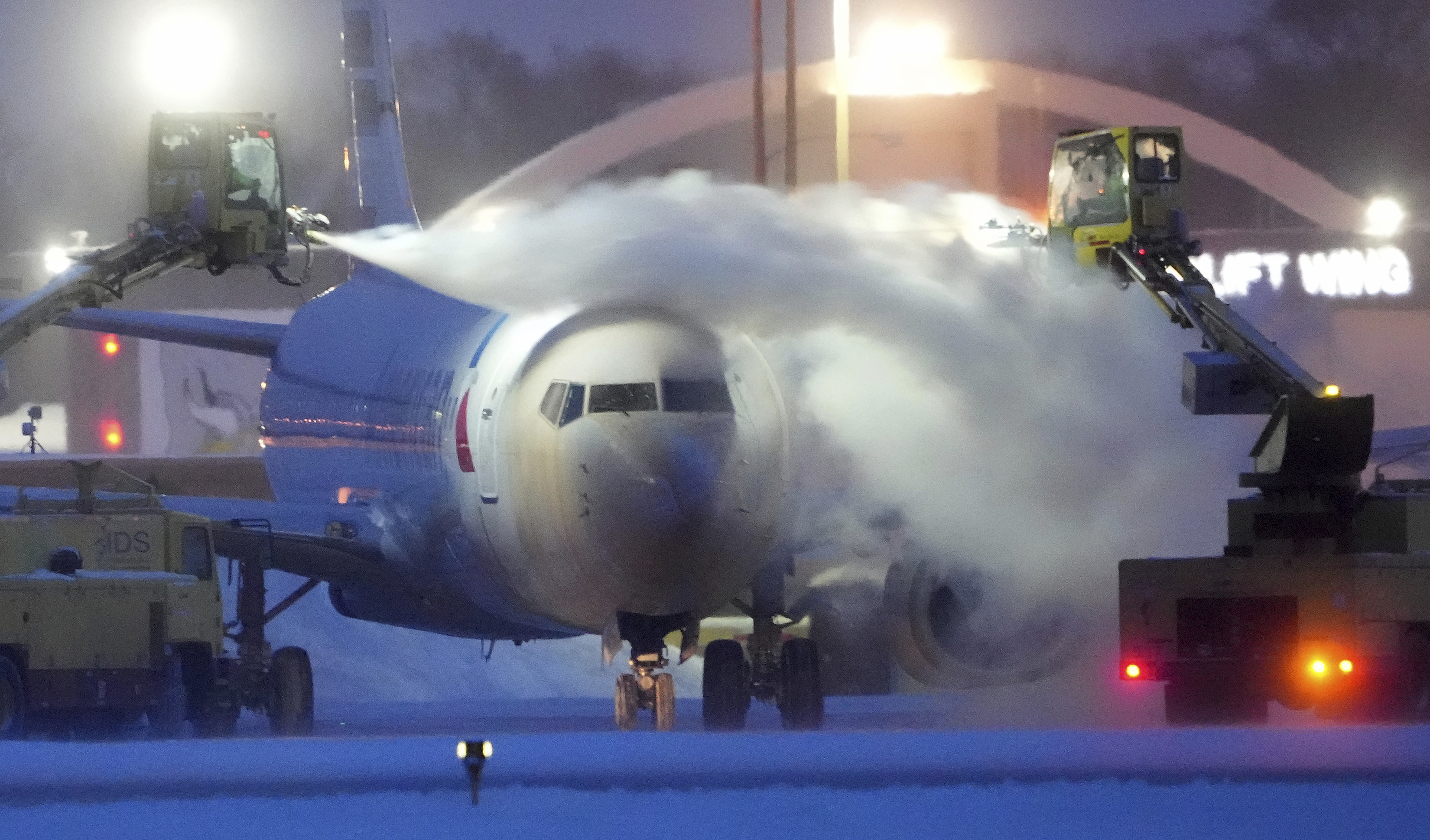 An American Airlines plane is de-iced as high winds whip around 7.5 inches of new snow at Minneapolis-St. Paul International Airport Thursday. Temperatures plunged far and fast Thursday as a winter storm formed ahead of Christmas weekend, promising heavy snow, ice, flooding and powerful winds across a broad swath of the country and complicating holiday travel.