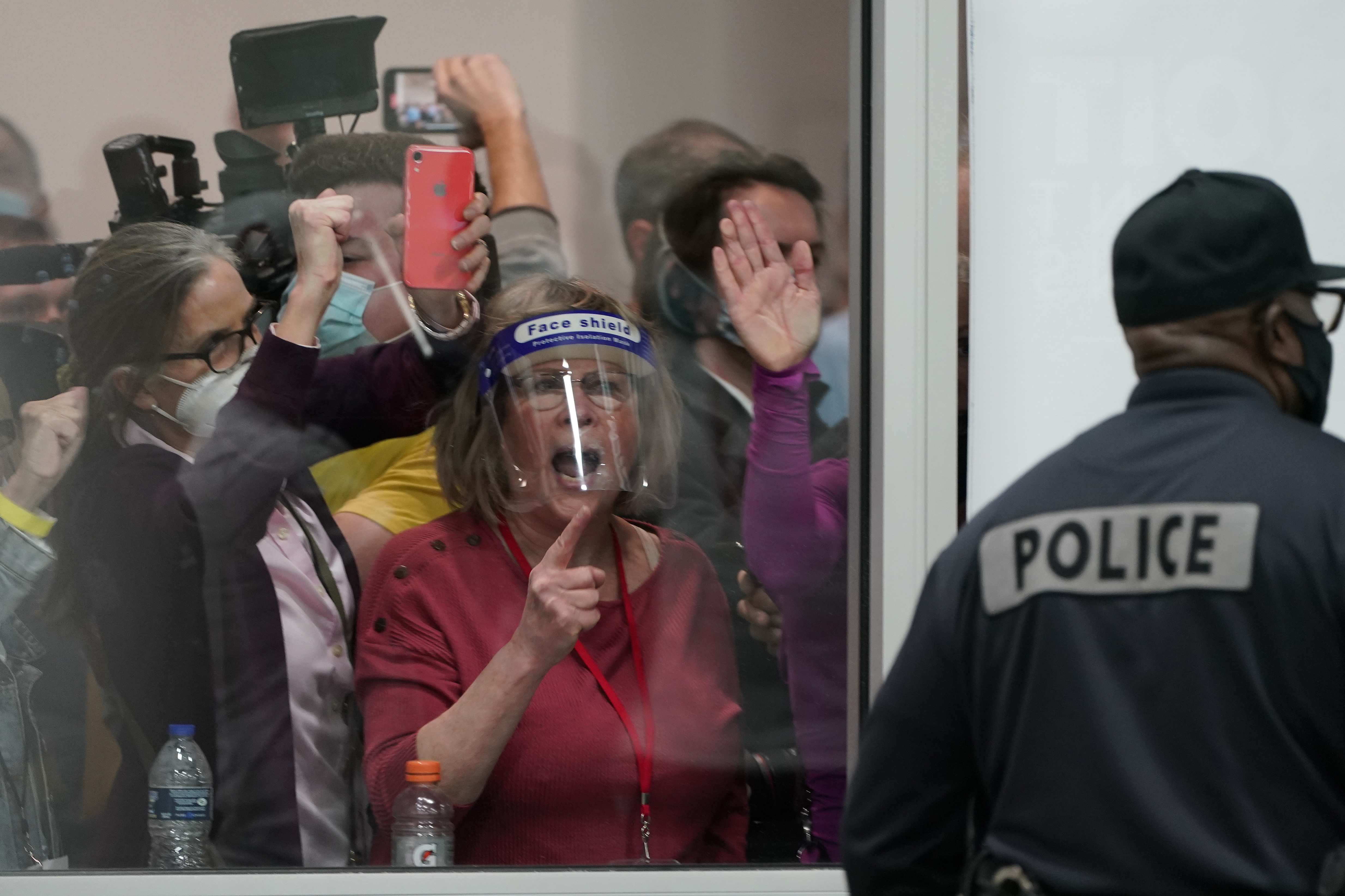 Election challengers yell as they look through the windows of the central counting board as police were helping to keep additional challengers from entering due to overcrowding, in Detroit, Nov. 4, 2020. 