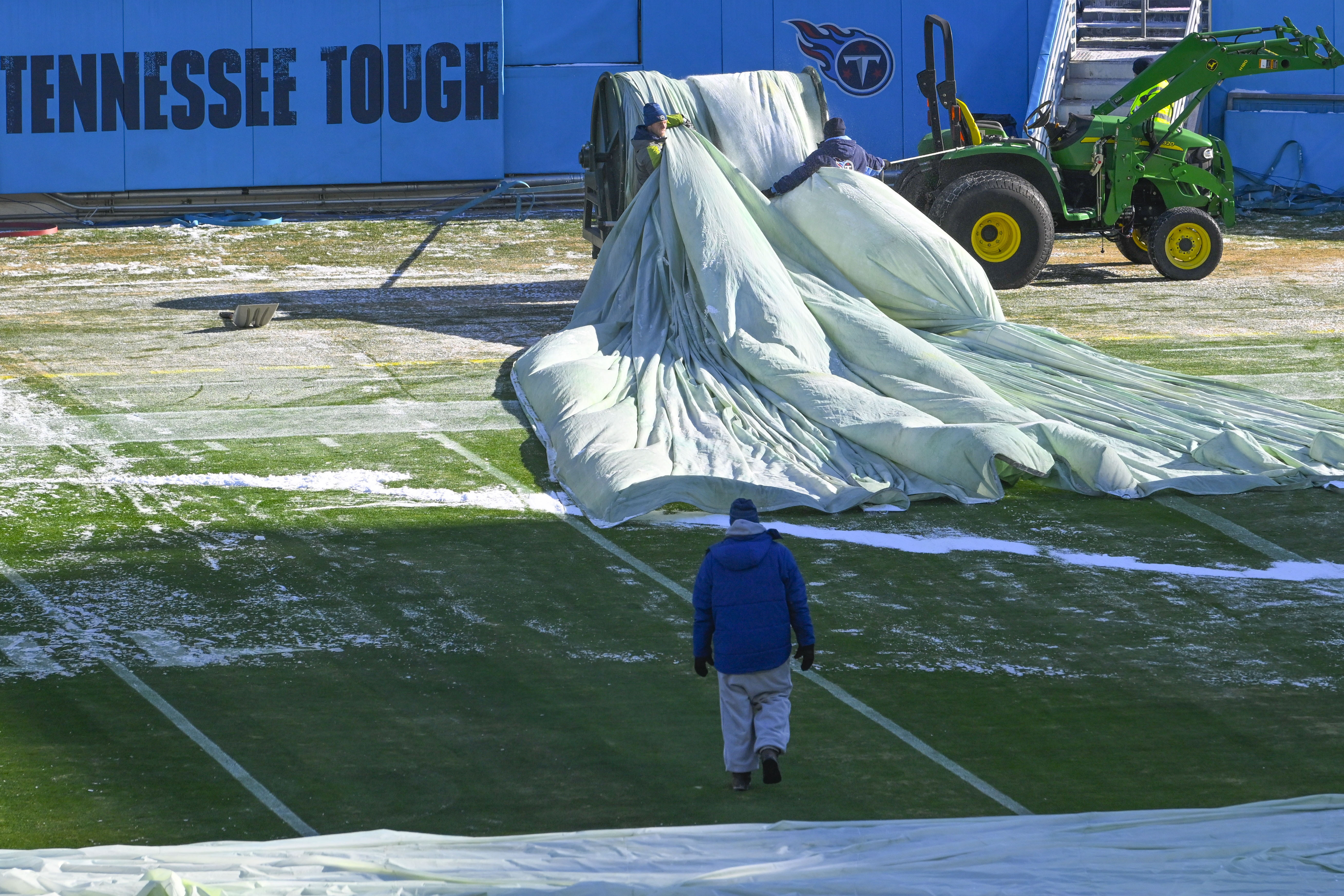 Crews remove tarps that covered the field overnight before an NFL football game between the Tennessee Titans and the Houston Texans, Saturday, Dec. 24, 2022, in Nashville, Tenn. Extreme cold weather has hit the region.