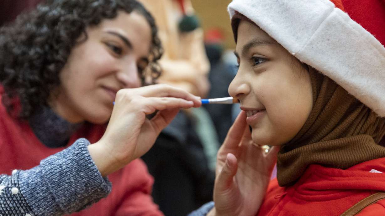Samar Al Ibrahim paints the face of Zahraa Neamh, 9, at the Utah Refugee Connection “Celebration of Light” at Lincoln Elementary School in South Salt Lake on Saturday, Dec. 17.