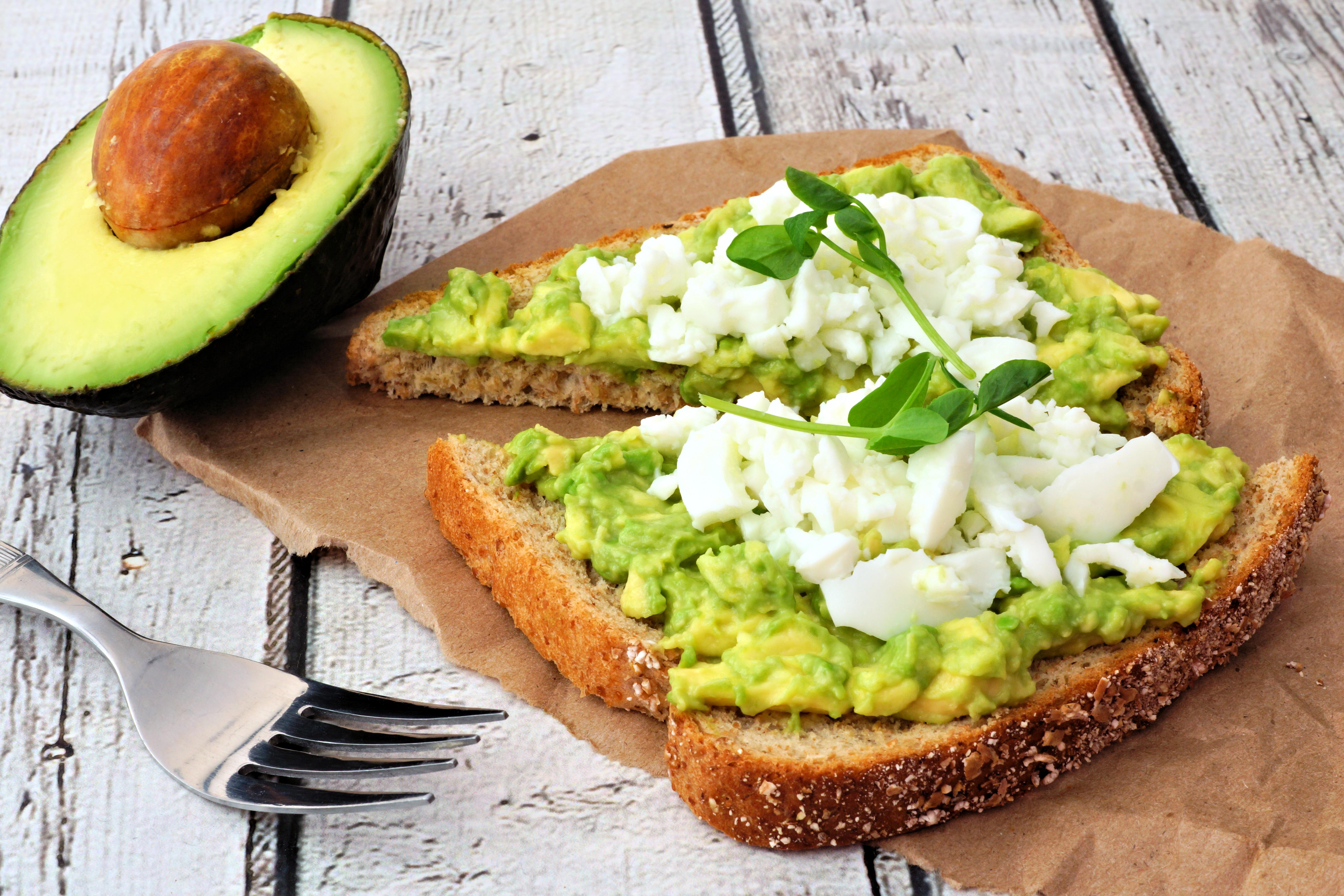 Avocado toast with egg whites and pea shoots on paper against a white wood background.