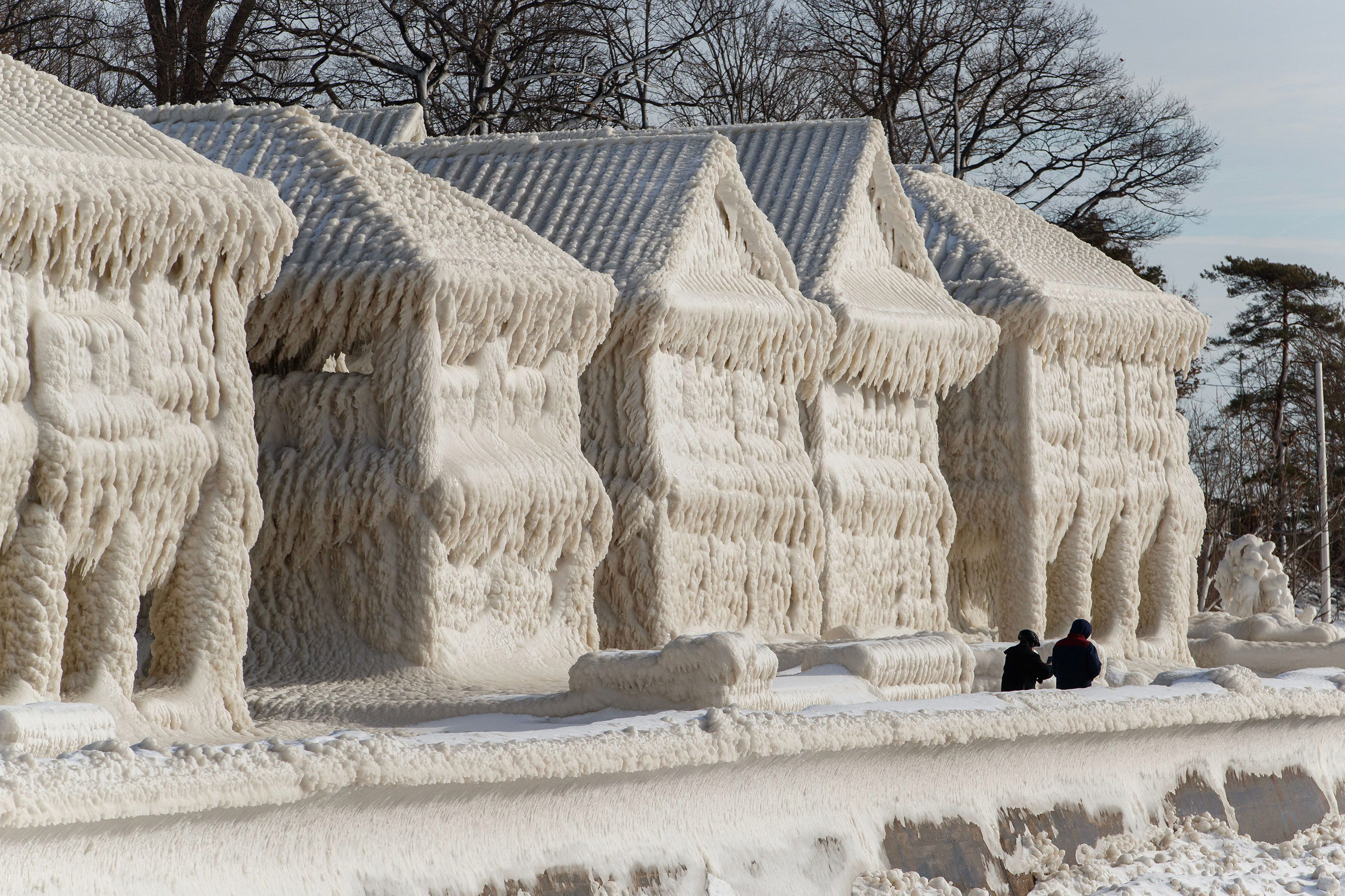 People walk by homes covered in ice at the waterfront community of Crystal Beach in Fort Erie, Ontario, Canada, on Wednesday, following a massive snow storm that knocked out power in the area to thousands of residents. 