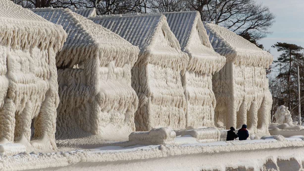 People walk by homes covered in ice at the waterfront community of Crystal Beach in Fort Erie, Ontario, Canada, on Wednesday, following a massive snow storm that knocked out power in the area to thousands of residents.