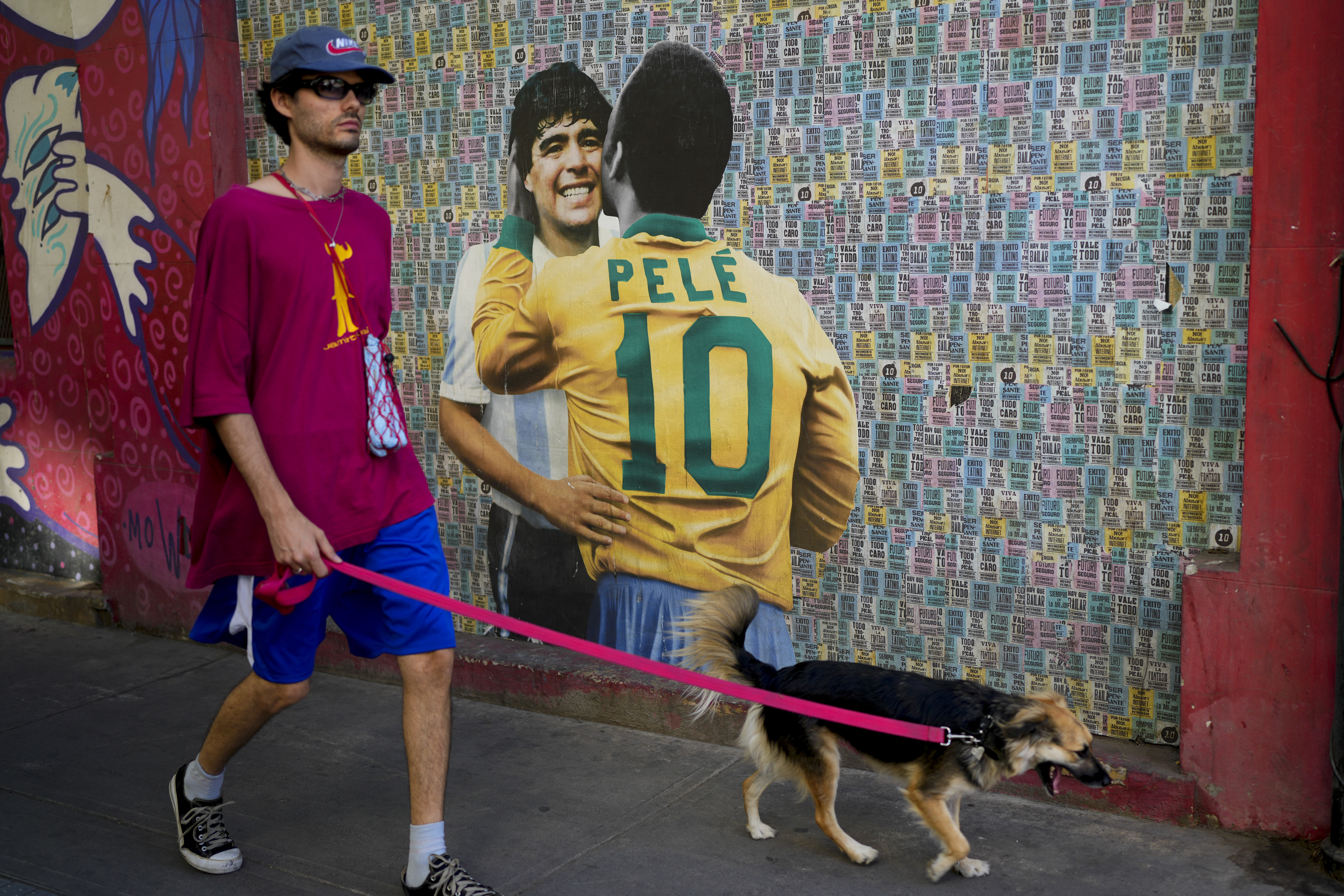 A man walks his dog walk past a mural showing Brazilian soccer legend Pele and Argentina late soccer star Diego Armando Maradona in Buenos Aires, Argentina, Thursday, Dec. 29, 2022. Pele, who won a record three World Cups has died at the age of 82. 