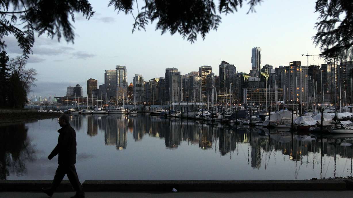 A man walks in Stanley Park as the skyline of Vancouver is reflected in water in Vancouver, British Columbia, on Feb. 5, 2010.