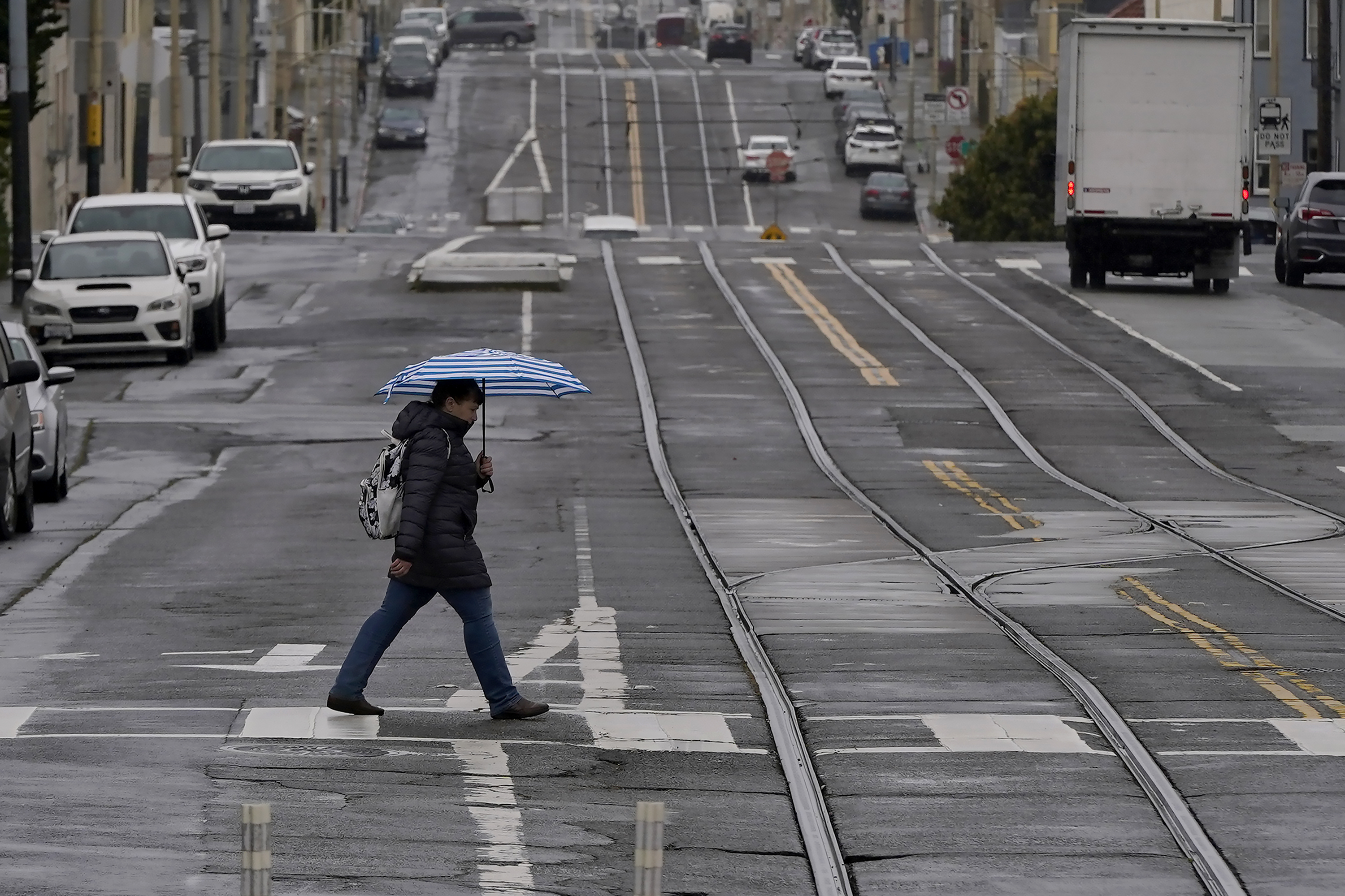 FILE - A pedestrian carries an umbrella while crossing a street in San Francisco, Thursday, April 14, 2022. A variety of new laws take effect Sunday, Jan. 1, 2023 that could have an impact on people's finances and, in some cases, their personal liberties. 