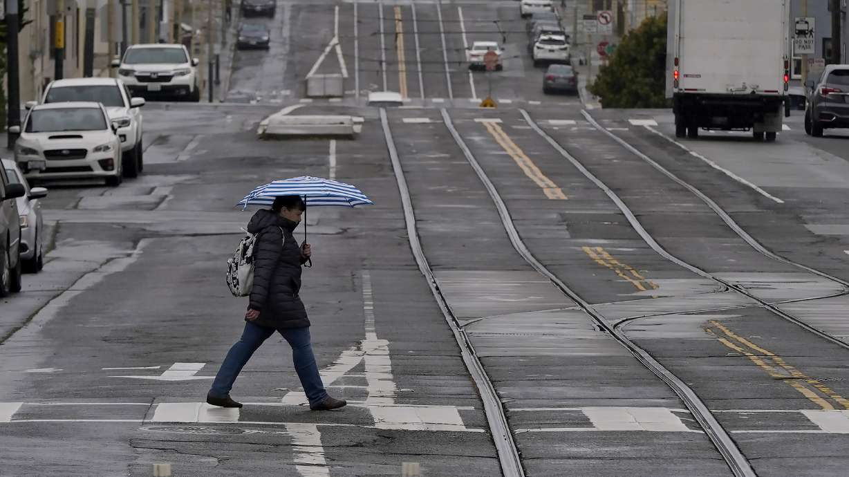 FILE - A pedestrian carries an umbrella while crossing a street in San Francisco, Thursday, April 14, 2022. A variety of new laws take effect Sunday, Jan. 1, 2023 that could have an impact on people's finances and, in some cases, their personal liberties.