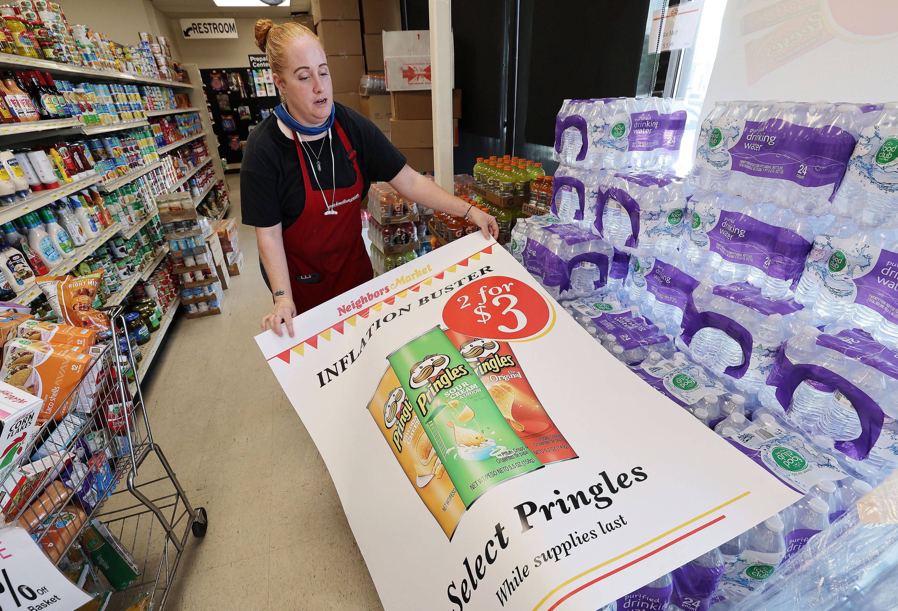 Wendy Buell prepares to hang an inflation buster product sign at Neighbors Market in North Salt Lake on Aug. 10, 2022. In spite of the tumult of the past year, the U.S. economy is closing out 2022 in much the same condition it was in at the end of last year, with inflation running around 7%, an ultra-tight labor market and vibrant levels of consumer spending.