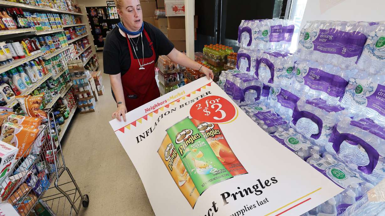 Wendy Buell prepares to hang an inflation buster product sign at Neighbors Market in North Salt Lake on Aug. 10, 2022. In spite of the tumult of the past year, the U.S. economy is closing out 2022 in much the same condition it was in at the end of last year, with inflation running around 7%, an ultra-tight labor market and vibrant levels of consumer spending.
