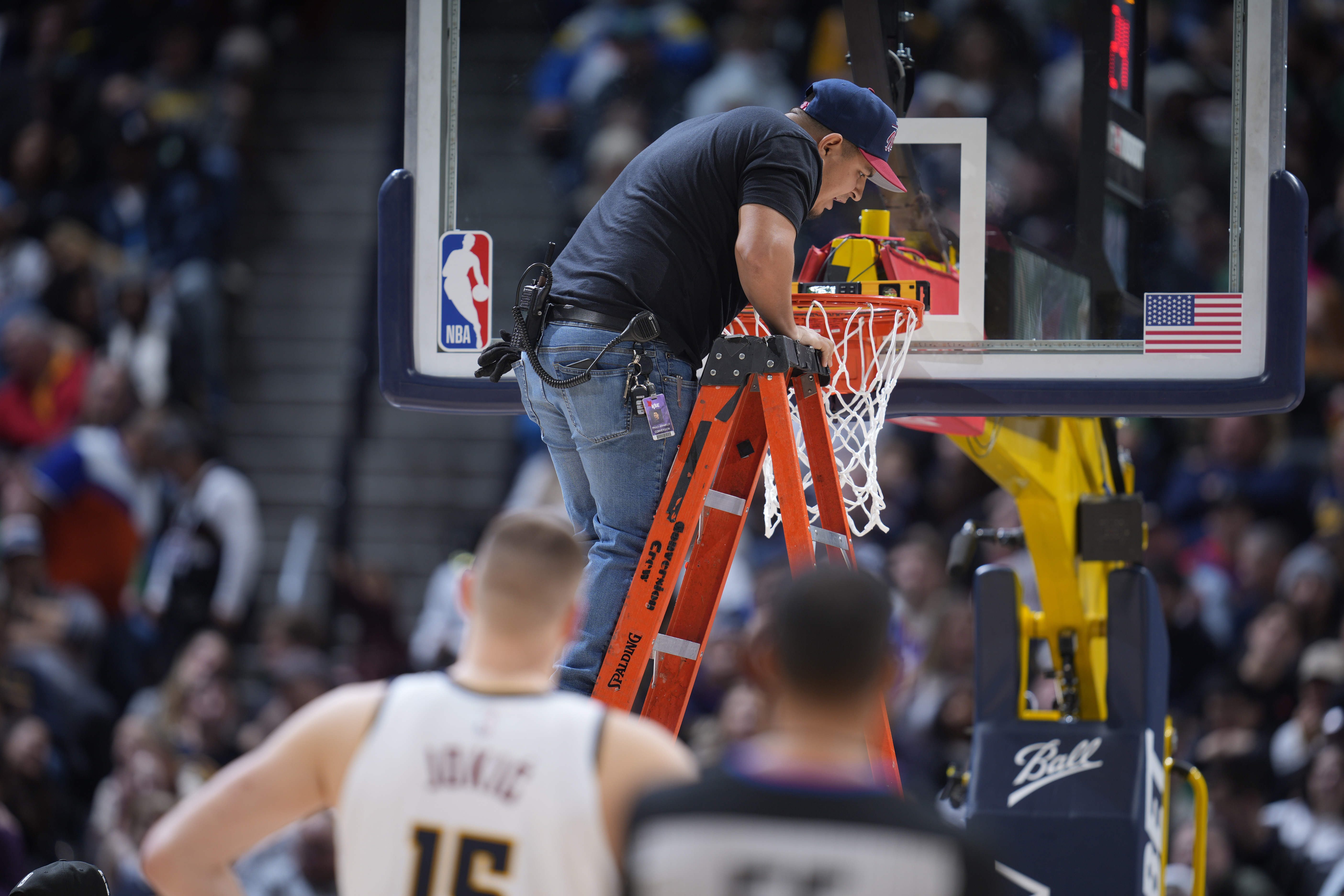 A worker uses a level to check the rim after it was bent by a dunk by Boston Celtics center Robert Williams III in the second half of an NBA basketball game against the Denver Nuggets, Sunday, Jan. 1, 2023, in Denver. 
