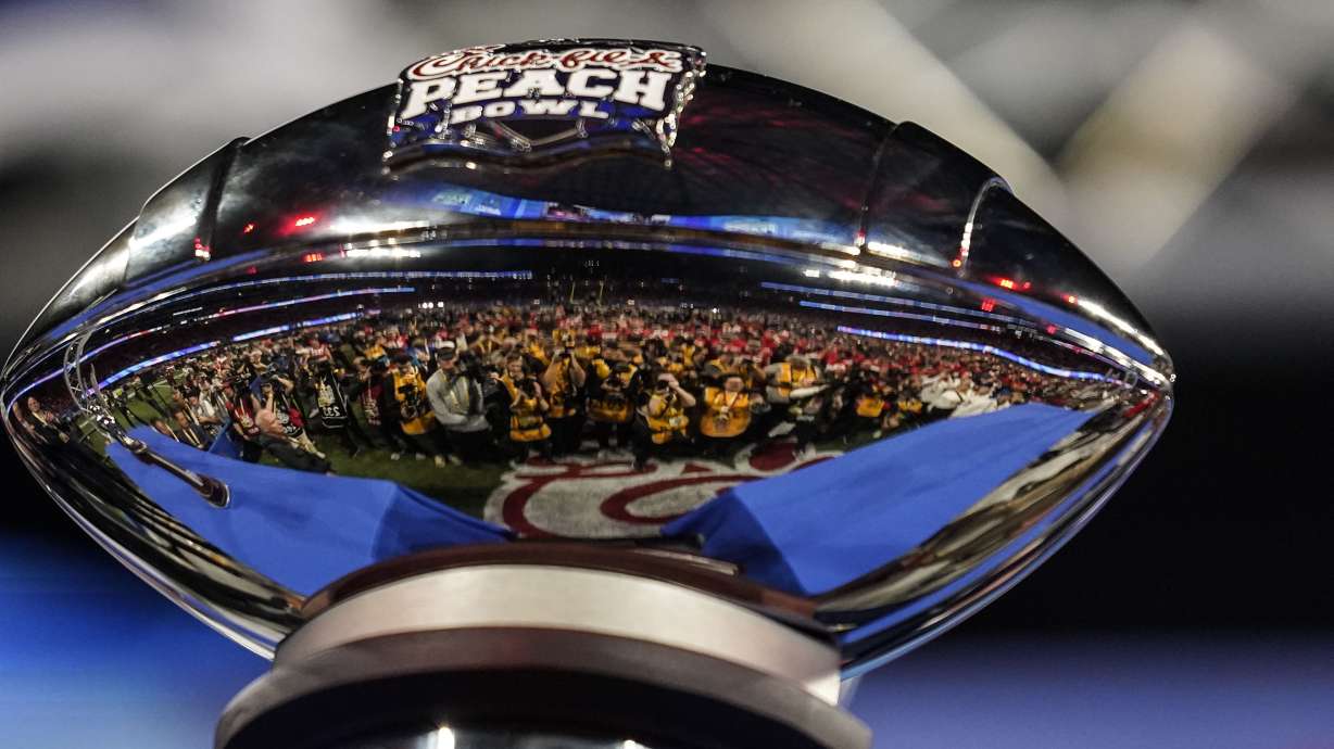 Photographers are reflected in the The George P. Crumbley Trophy after the Peach Bowl NCAA college football semifinal playoff game between Georgia and Ohio State, Sunday, Jan. 1, 2023, in Atlanta. Georgia won 42-41.