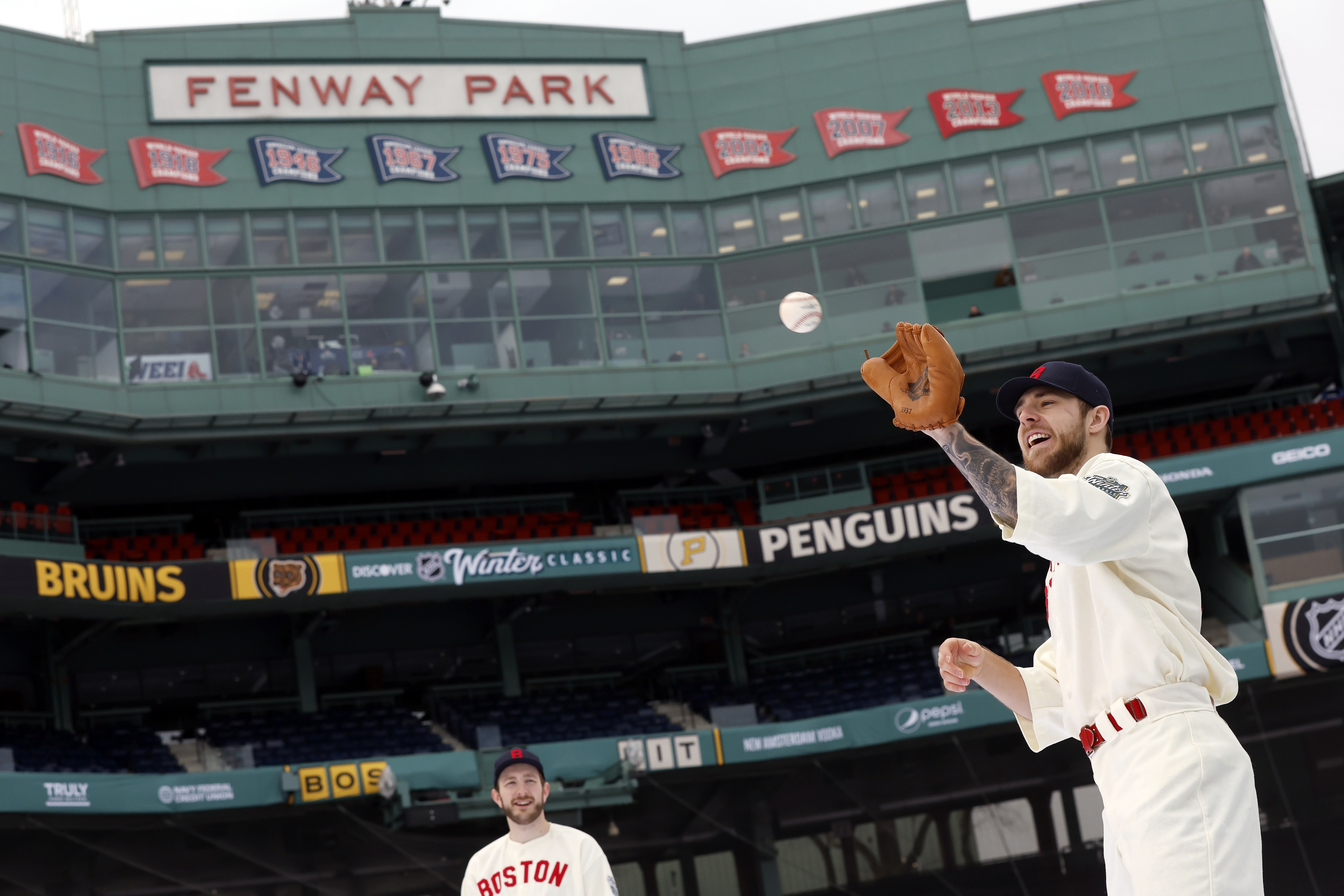 Boston Bruins' A.J. Greer, right, plays catch in a vintage Boston Red Sox uniform before the NHL Winter Classic hockey game against the Pittsburgh Penguins, Monday, Jan. 2, 2023, at Fenway Park in Boston.