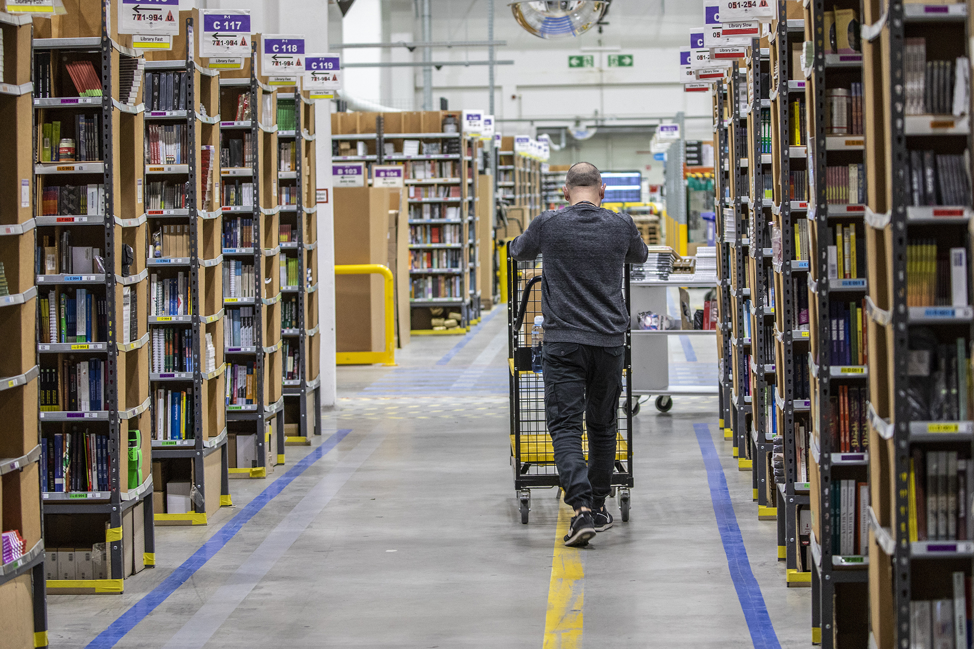 A worker pushes a cart laden with ordered items among shelves at an Amazon warehouse in November 2021 in Brieselang, Germany. Amazon will lay off 17,000 employees according to the Wall Street Journal, citing unnamed sources. 