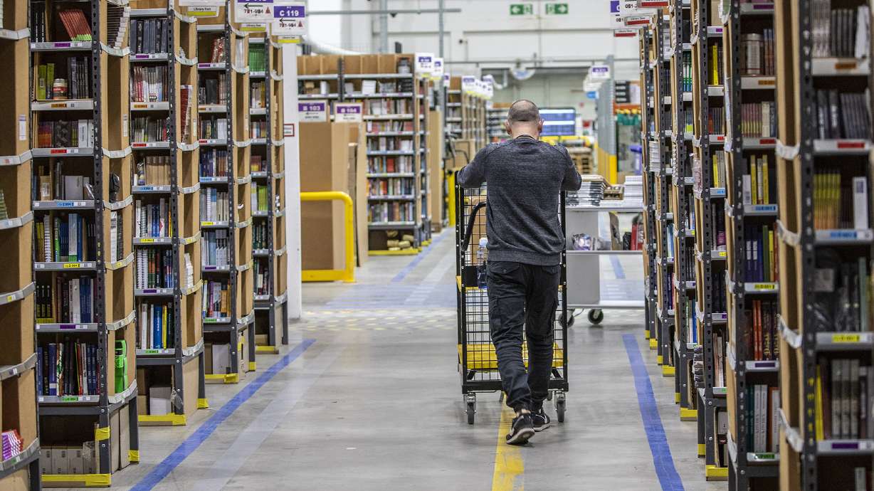 A worker pushes a cart laden with ordered items among shelves at an Amazon warehouse in November 2021 in Brieselang, Germany. Amazon will lay off 17,000 employees according to the Wall Street Journal, citing unnamed sources.