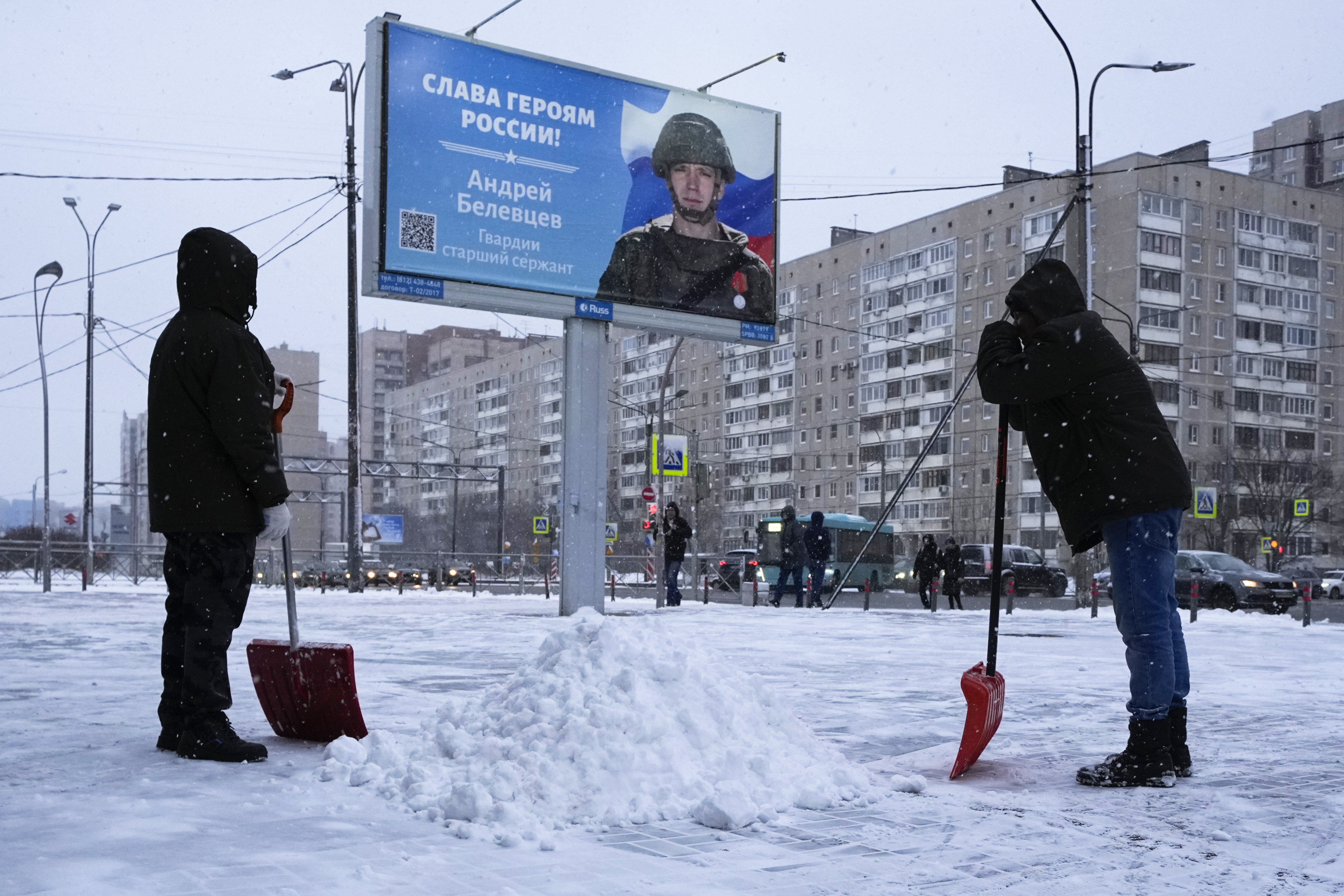 Workers clear the snow next to a billboard with a portrait of a Russian soldier awarded for action in Ukraine and the words "Glory to the heroes of Russia" in St. Petersburg, Russia, Tuesday. Russian President Vladimir Putin has ordered his armed forces to observe a 36-hour unilateral cease-fire in Ukraine this weekend for the Orthodox Christmas holiday.