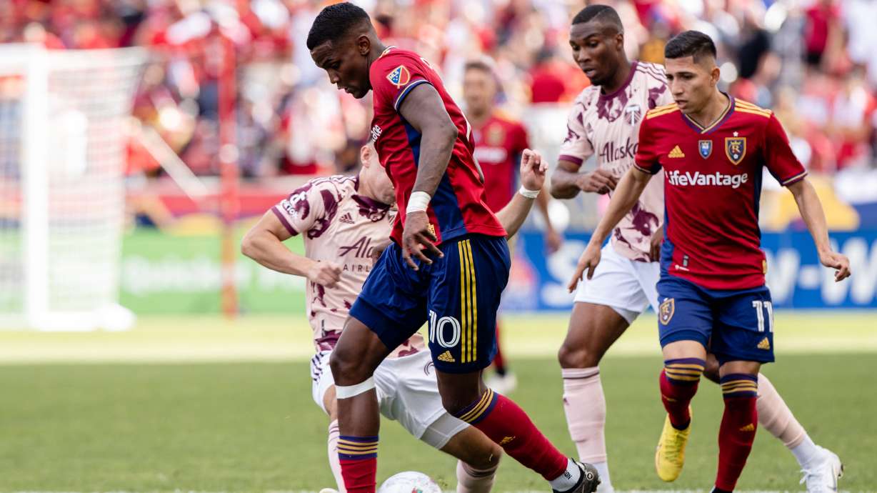 Sergio Cordova dribbles away from Portland defenders as Jefferson Savarino looks on at America First Field.