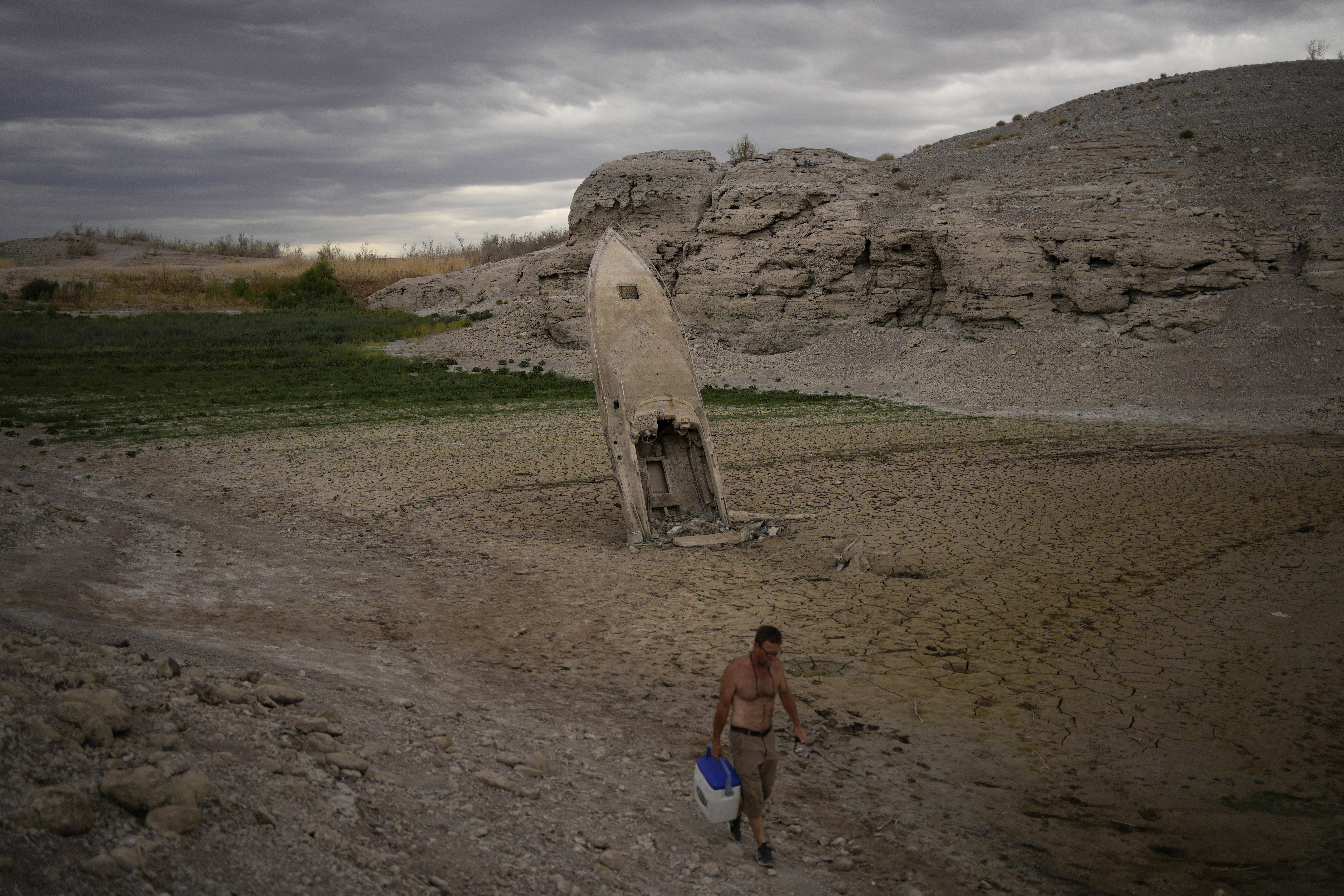 A man walks by a formerly sunken boat standing upright into the air with its stern buried in the mud along the shoreline of Lake Mead amid a drought at the Lake Mead National Recreation Area, June 22, 2022. Costly weather disasters kept raining down on America last year.