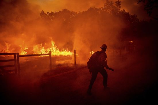 A firefighter runs to extinguish flames as the Oak Fire crosses Darrah Road in Mariposa County, Calif., on July 22, 2022. Costly weather disasters kept raining down on America last year, pounding the nation with 18 climate extremes that caused at least $1 billion in damage each, totaling more than $165 billion, federal climate scientists calculated Tuesday.