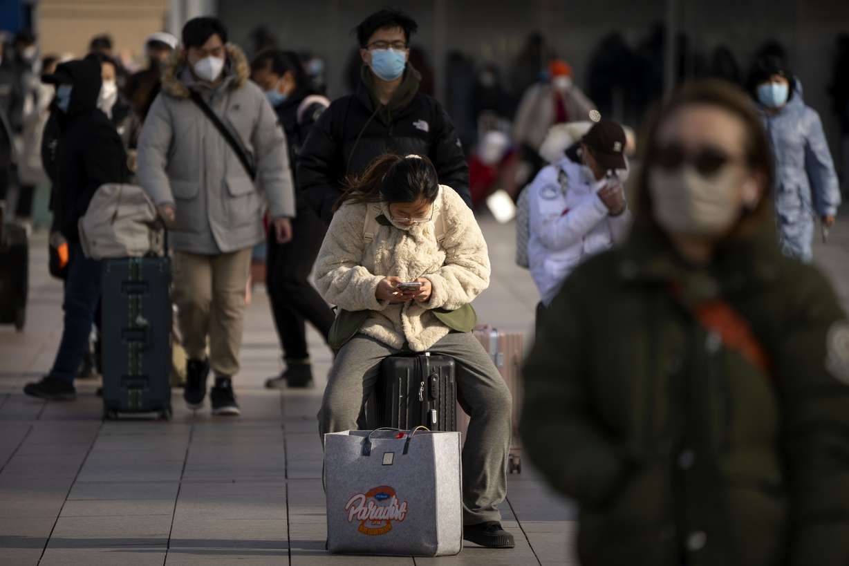 A traveler sits on her suitcase outside the entrance of the Beijing Railway Station in Beijing, Saturday. Millions of Chinese are expected to travel during the Lunar New Year holiday period this year.
