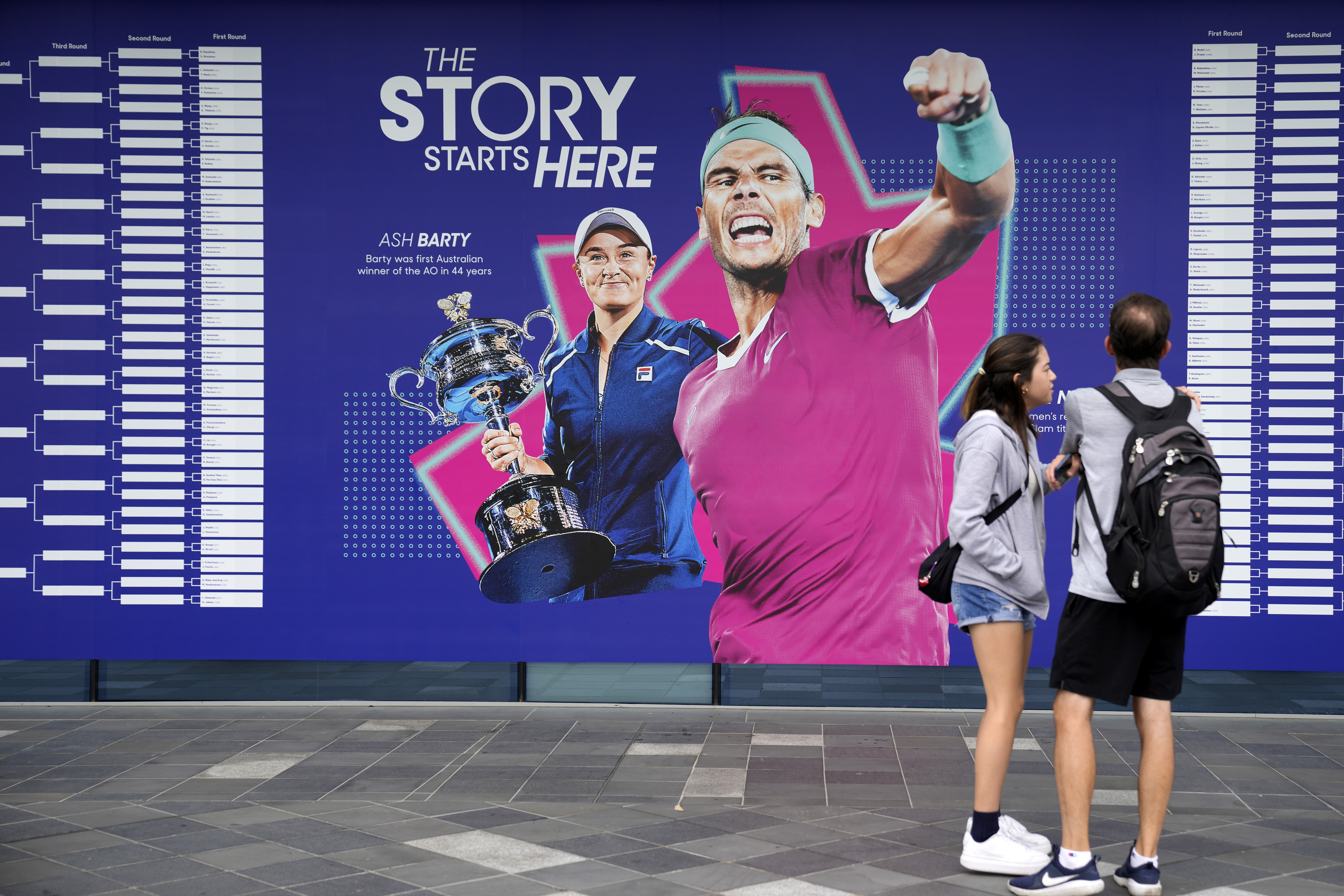 Spectators stand by an illustration of 2022 champions Ash Barty and Rafael Nadal, ahead of first round matches at the Australian Open tennis championship in Melbourne, Australia, Monday, Jan. 16, 2023. 