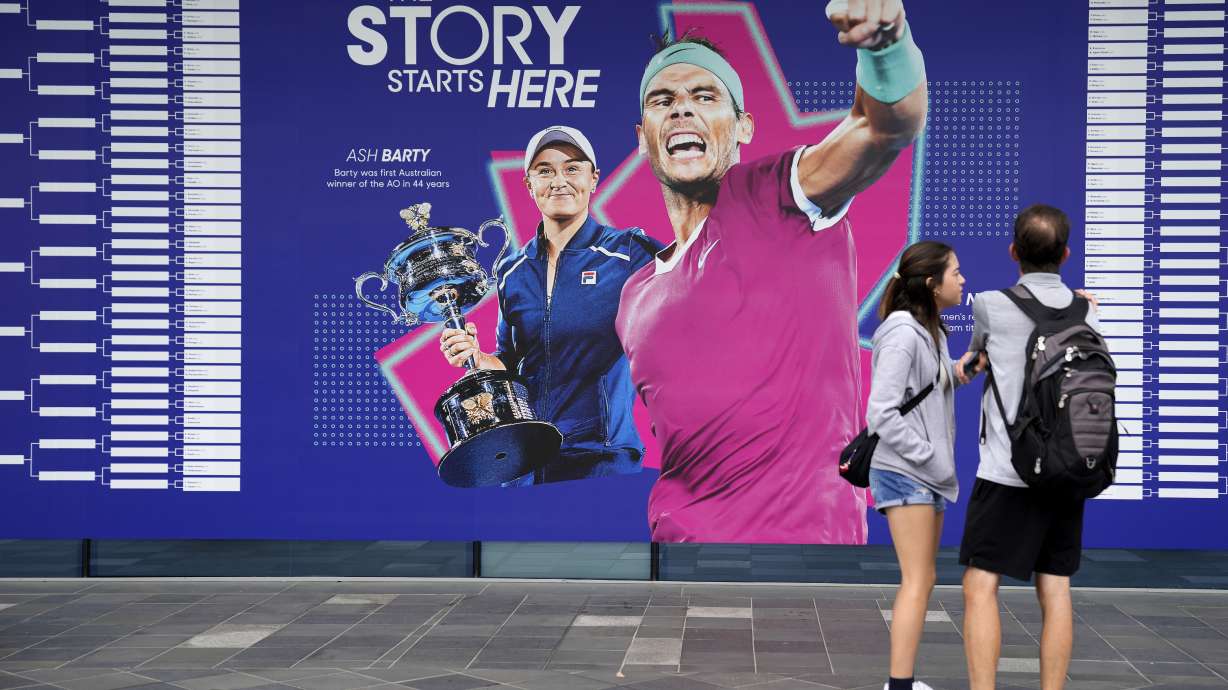 Spectators stand by an illustration of 2022 champions Ash Barty and Rafael Nadal, ahead of first round matches at the Australian Open tennis championship in Melbourne, Australia, Monday, Jan. 16, 2023.
