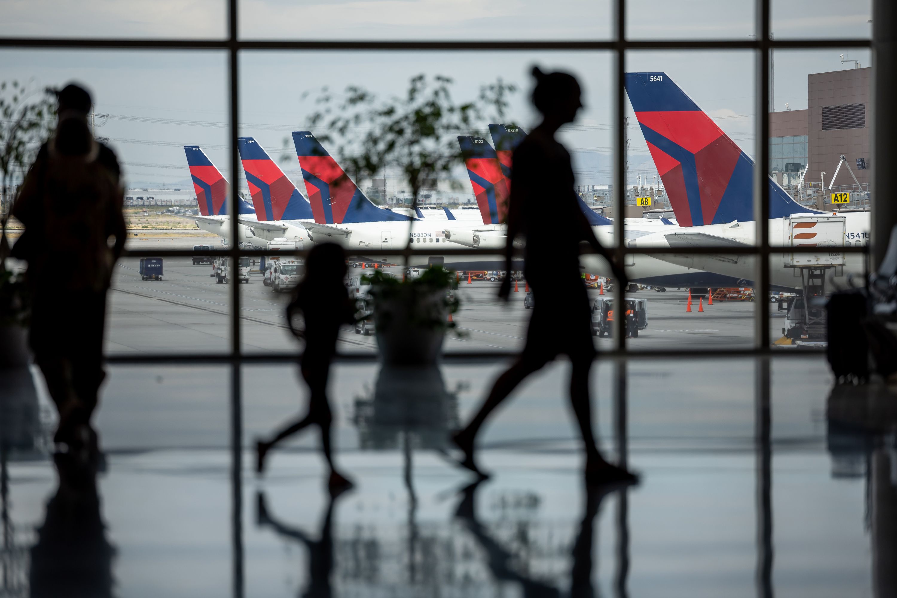 People walk through the baggage claim with Delta jets visible at their gates at the Salt Lake City International Airport in Salt Lake City on Aug. 2, 2022.