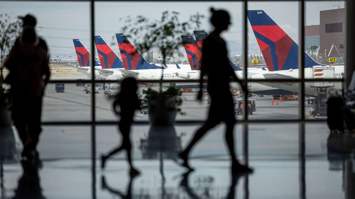People walk through the baggage claim with Delta jets visible at their gates at the Salt Lake City International Airport in Salt Lake City on Aug. 2, 2022.