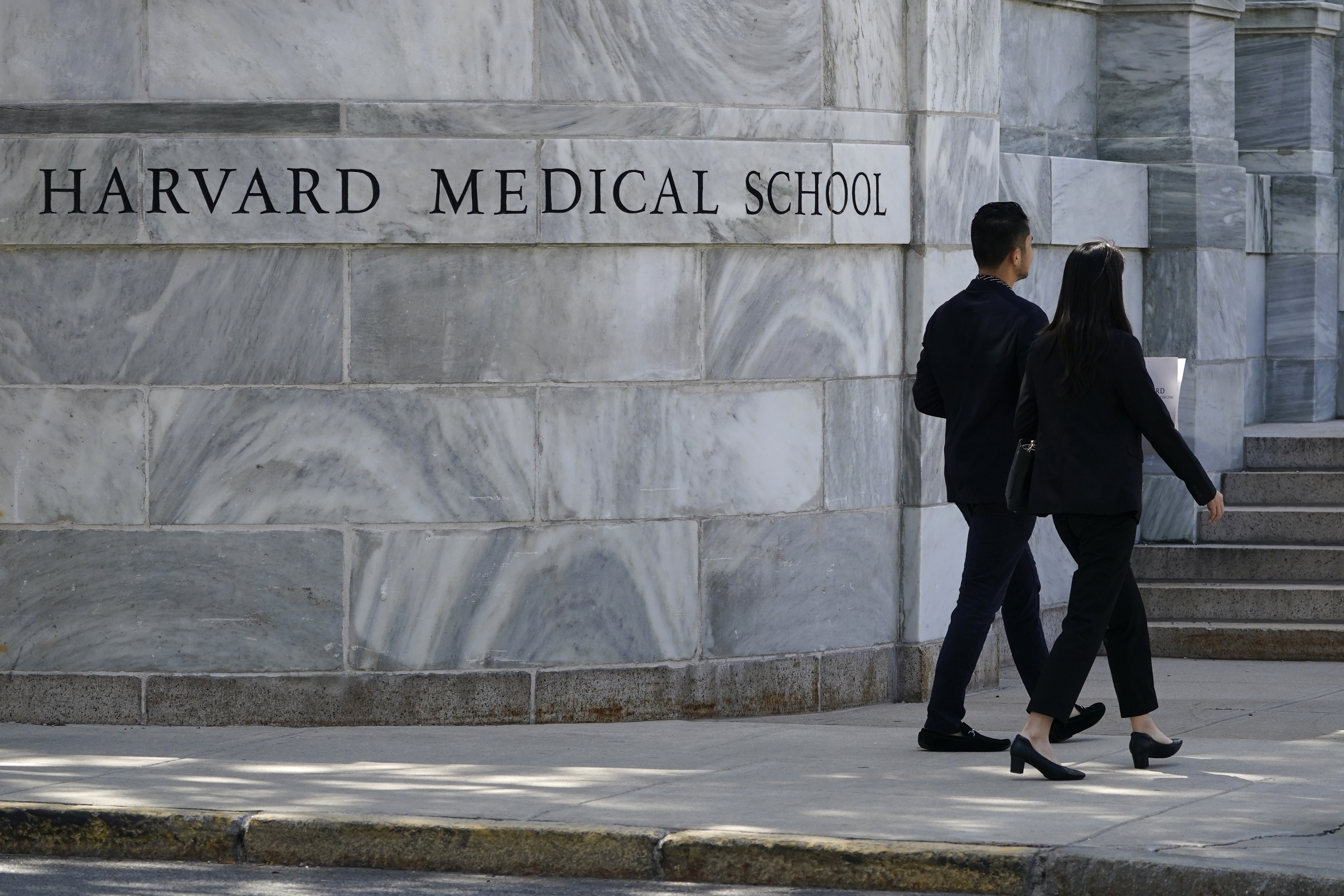 Pedestrians walk toward the Harvard Medical School, Aug. 18, 2022, in Boston. A former manager at the Harvard Medical School morgue, his wife and three other people have been indicted in connection with the theft and sale of human body parts.