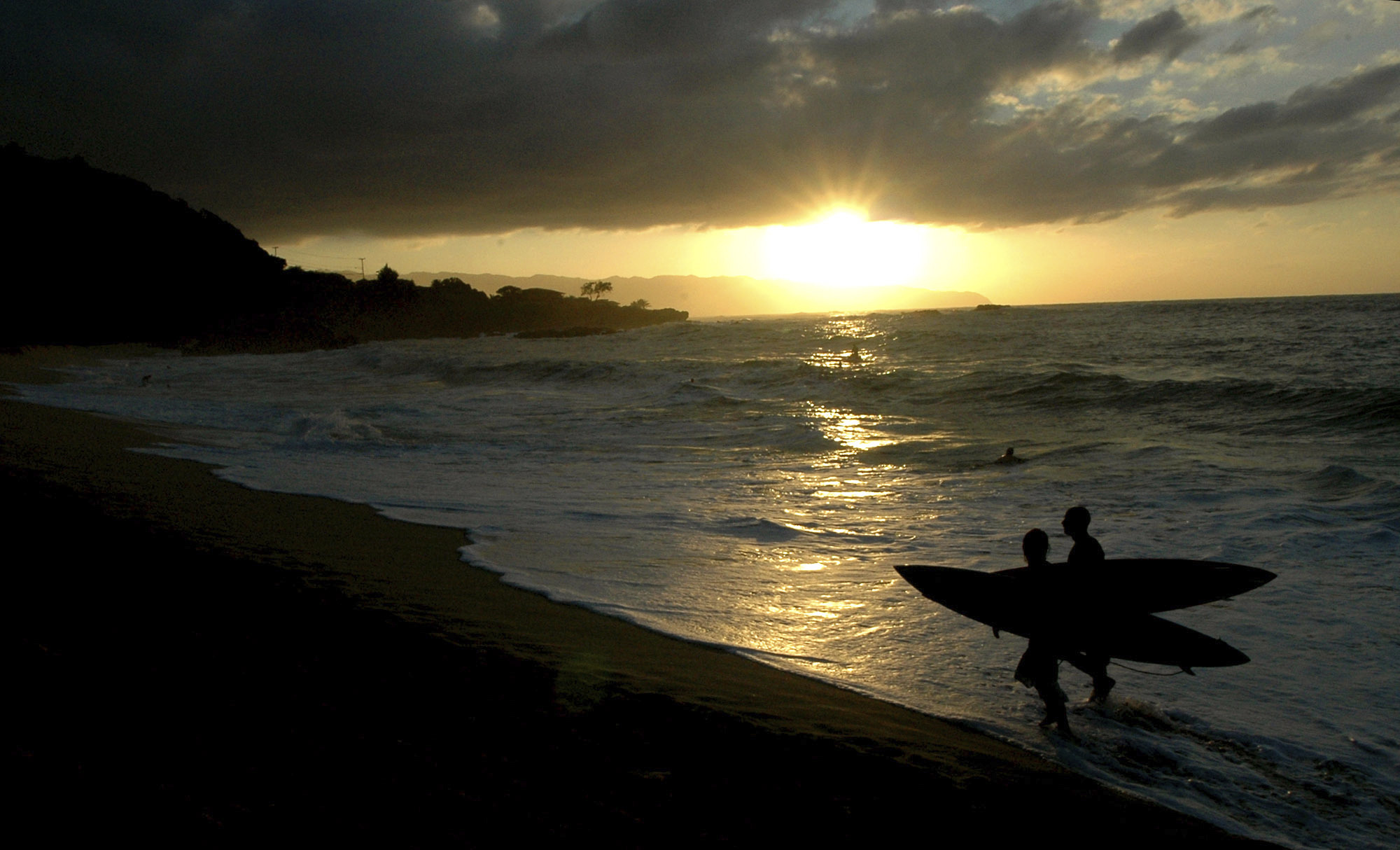 FILE - Participants in the In Memory of Eddie Aikau walk out of the ocean at sunset after the opening ceremony in Waimea Bay near Haleiwa, Hawaii, on Nov. 30, 2006. One of the world's most prestigious and storied surfing contests is expected to be held on Sunday, Jan. 22, 2023, in Hawaii for the first time in seven years - if conditions are right. And female surfers will be competing alongside the men for the first time in the 39-year history of The Eddie Aikau Big Wave Invitational.