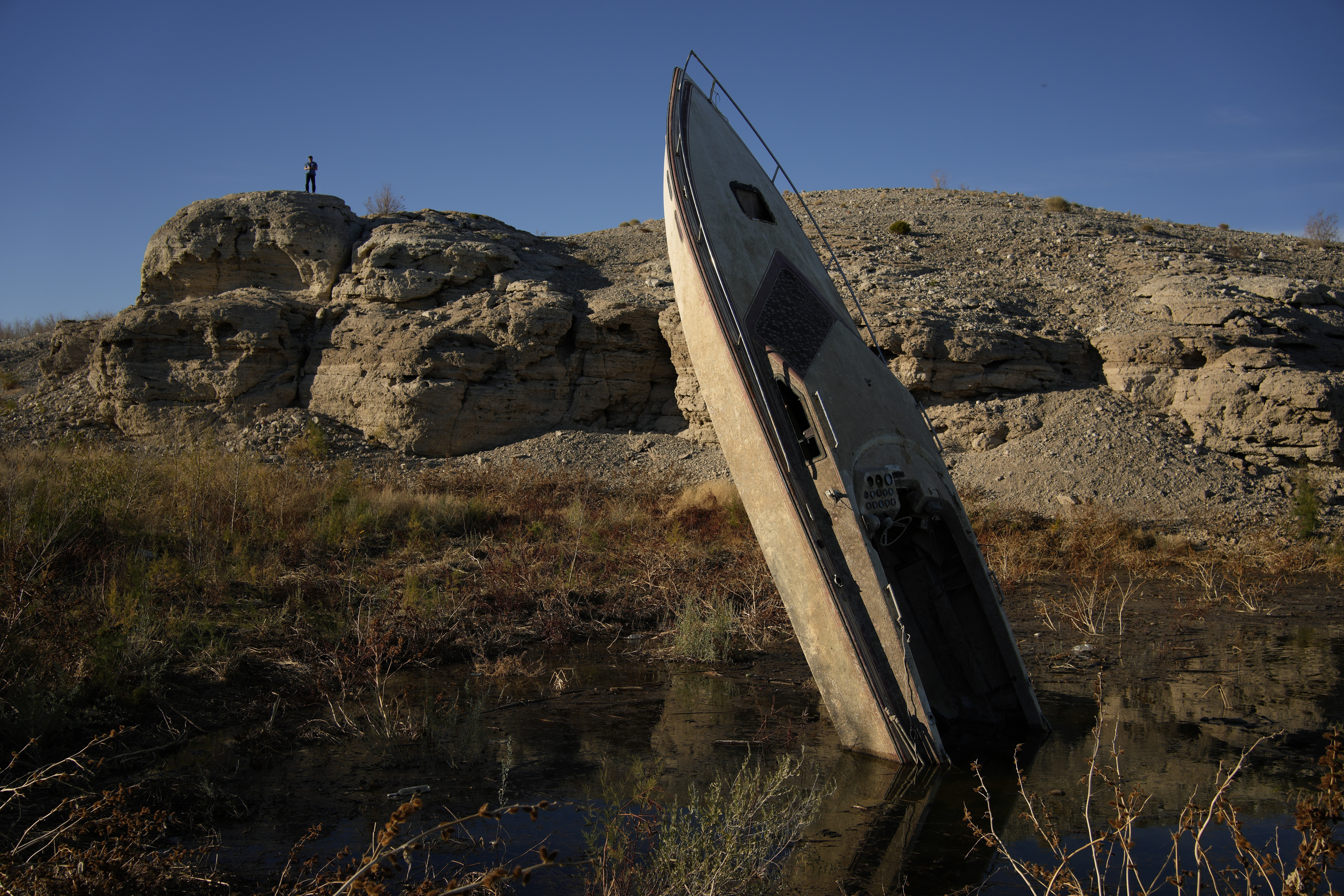 A man stands on a hill overlooking a formerly sunken boat along the shoreline of Lake Mead Jan. 27, near Boulder City, Nevada. Competing priorities, outsized demands and the federal government's retreat from a threatened deadline all combined to thwart a voluntary deal on how to drastically cut water use from the Colorado River.