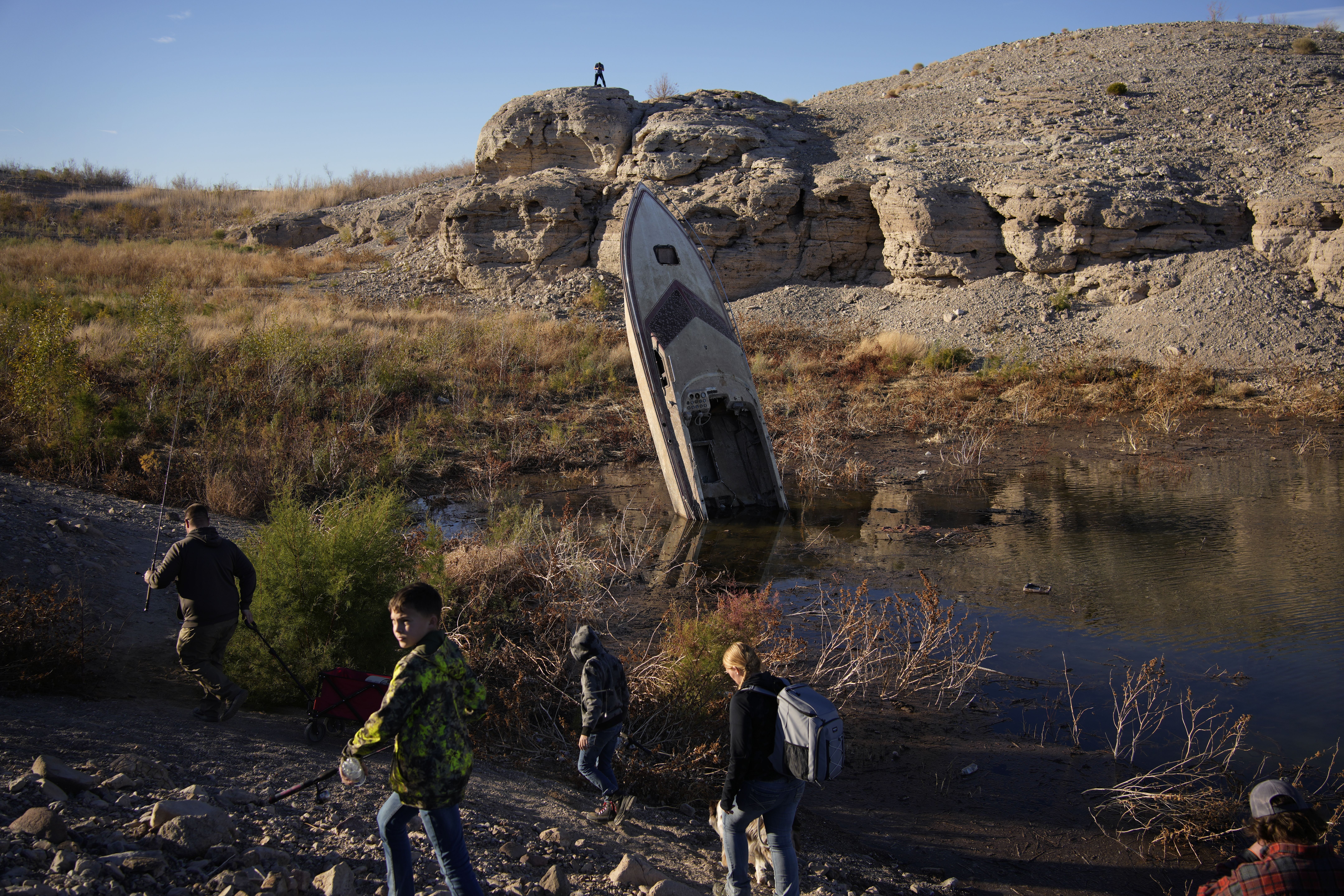 People walk by a formerly sunken boat standing upright into the air with its stern buried in the mud along the shoreline of Lake Mead on Jan. 27, near Boulder City, Nevada. Utah Gov. Spencer Cox said Thursday that he's a "little more optimistic" that all of the Colorado River states can come to an agreement on a plan to reduce water use.